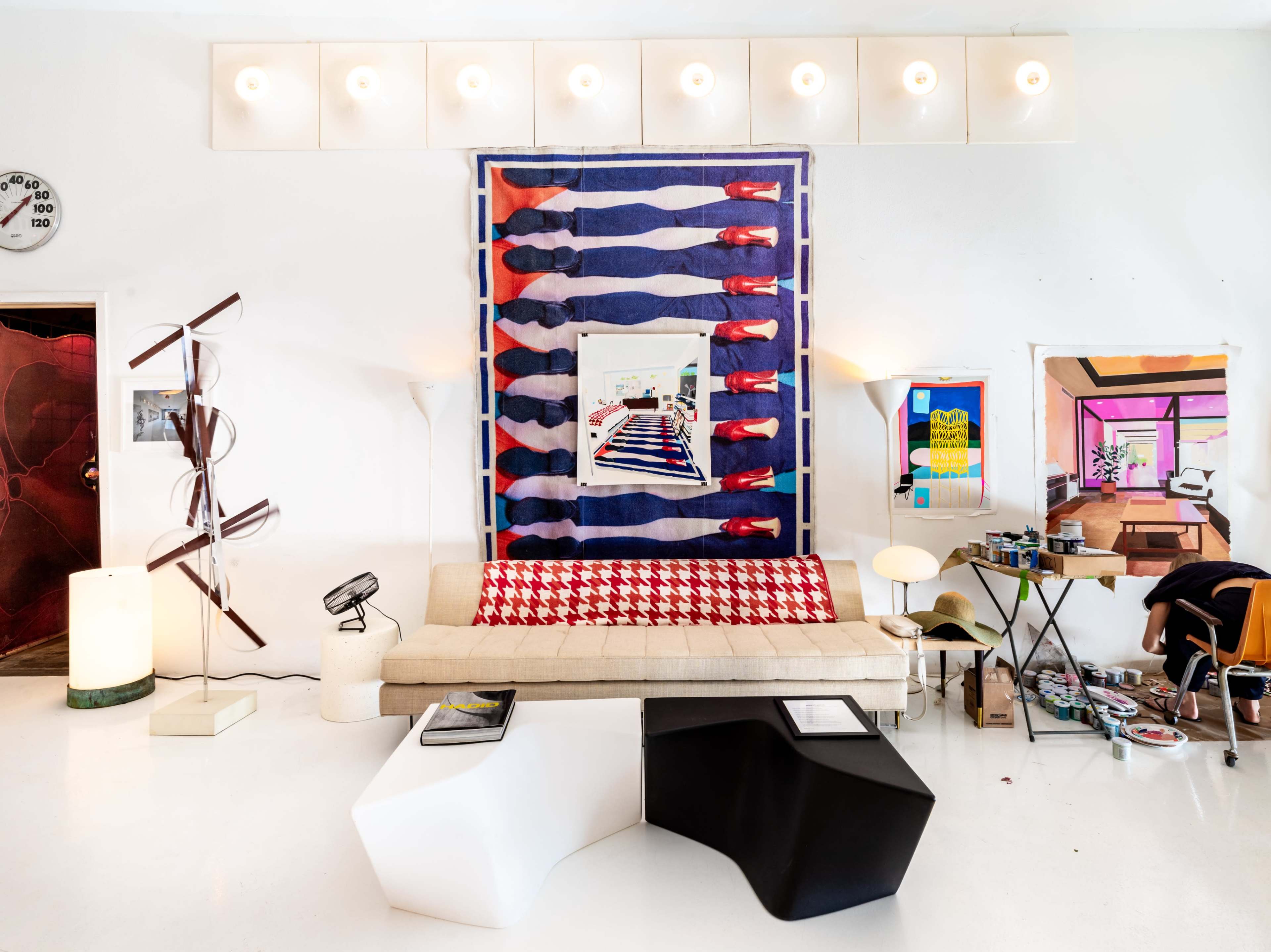 The image features a modern living room with a white sofa, colorful wall art, unique light fixtures, and various decor items scattered around.