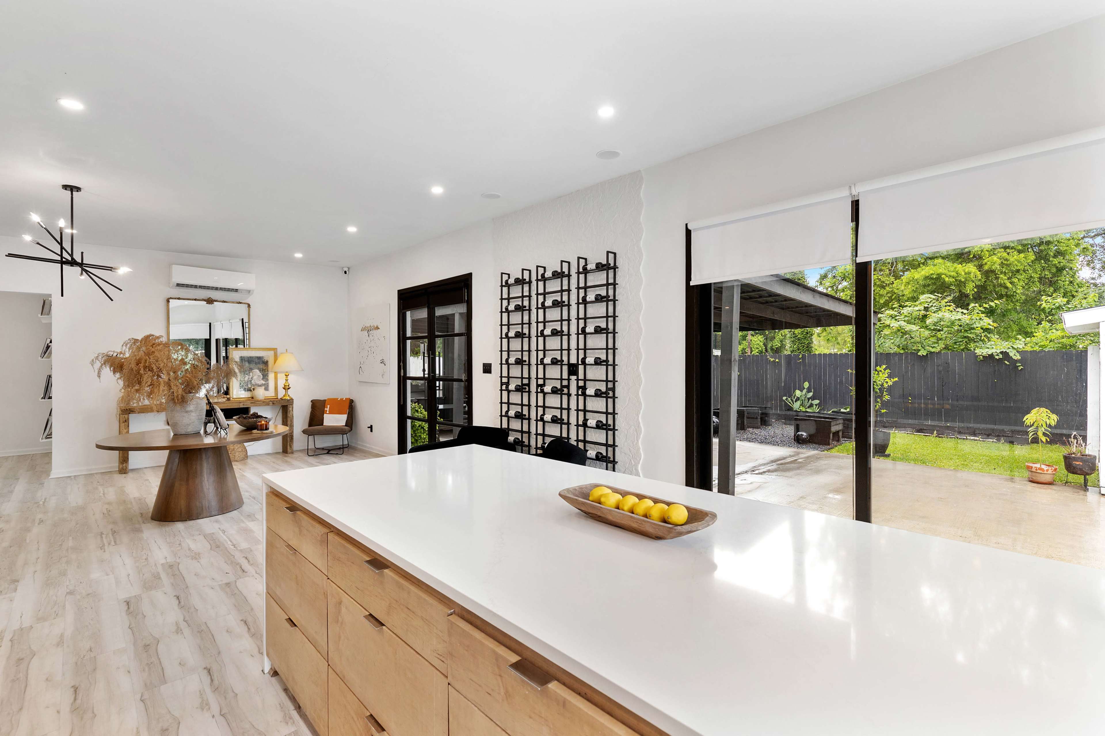 The image shows a modern, open-concept living space with a kitchen featuring a central island, a dining area, and large sliding doors leading to an outdoor patio.