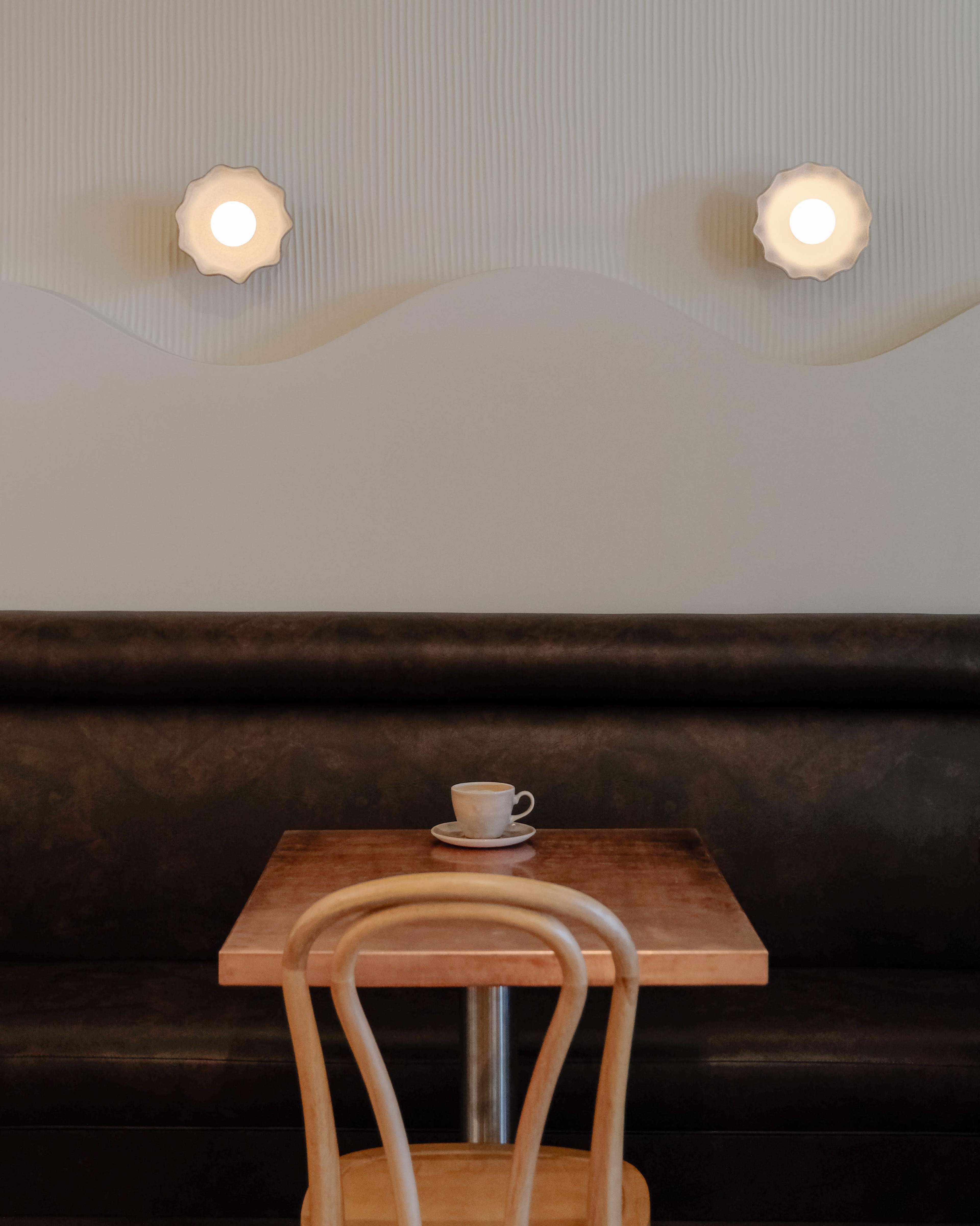 A simple wooden table with a cup of coffee sits in front of a wall featuring two round light fixtures.