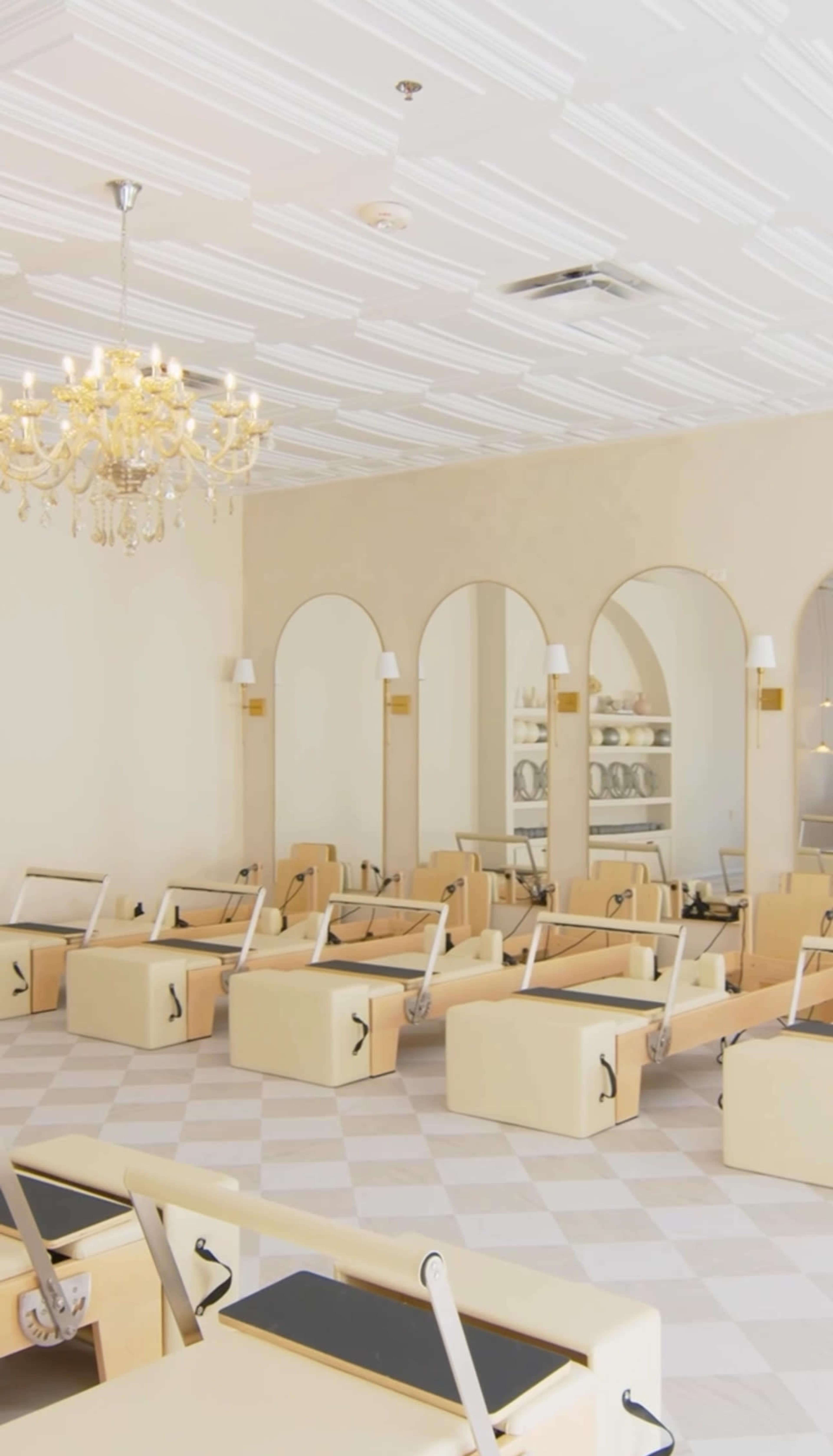 The image shows a spacious pilates studio with beige reformer machines arranged in rows and large mirrors on the walls.