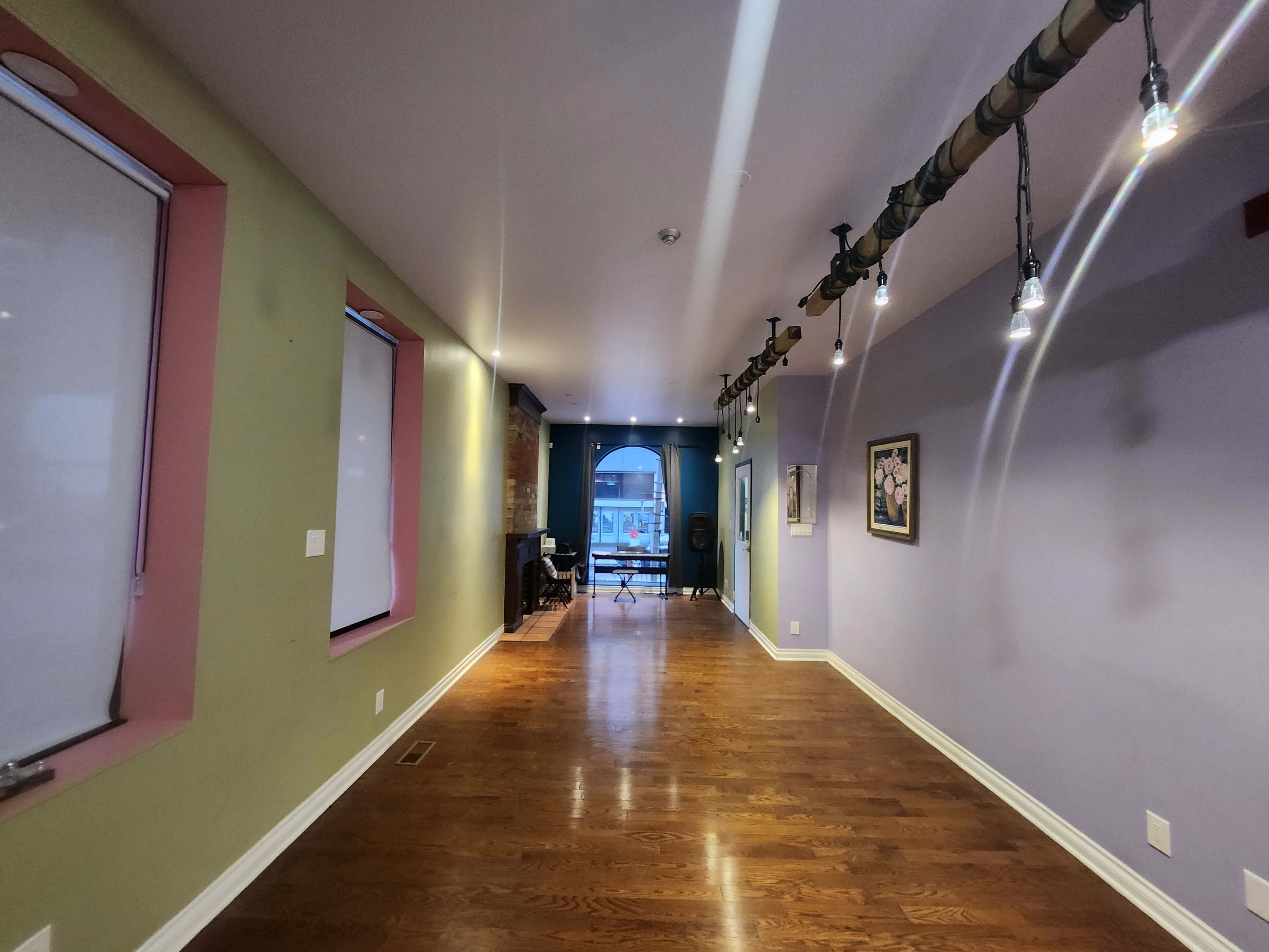 A long hallway with wooden flooring, colorful walls, and track lighting, leading to a window at the far end.