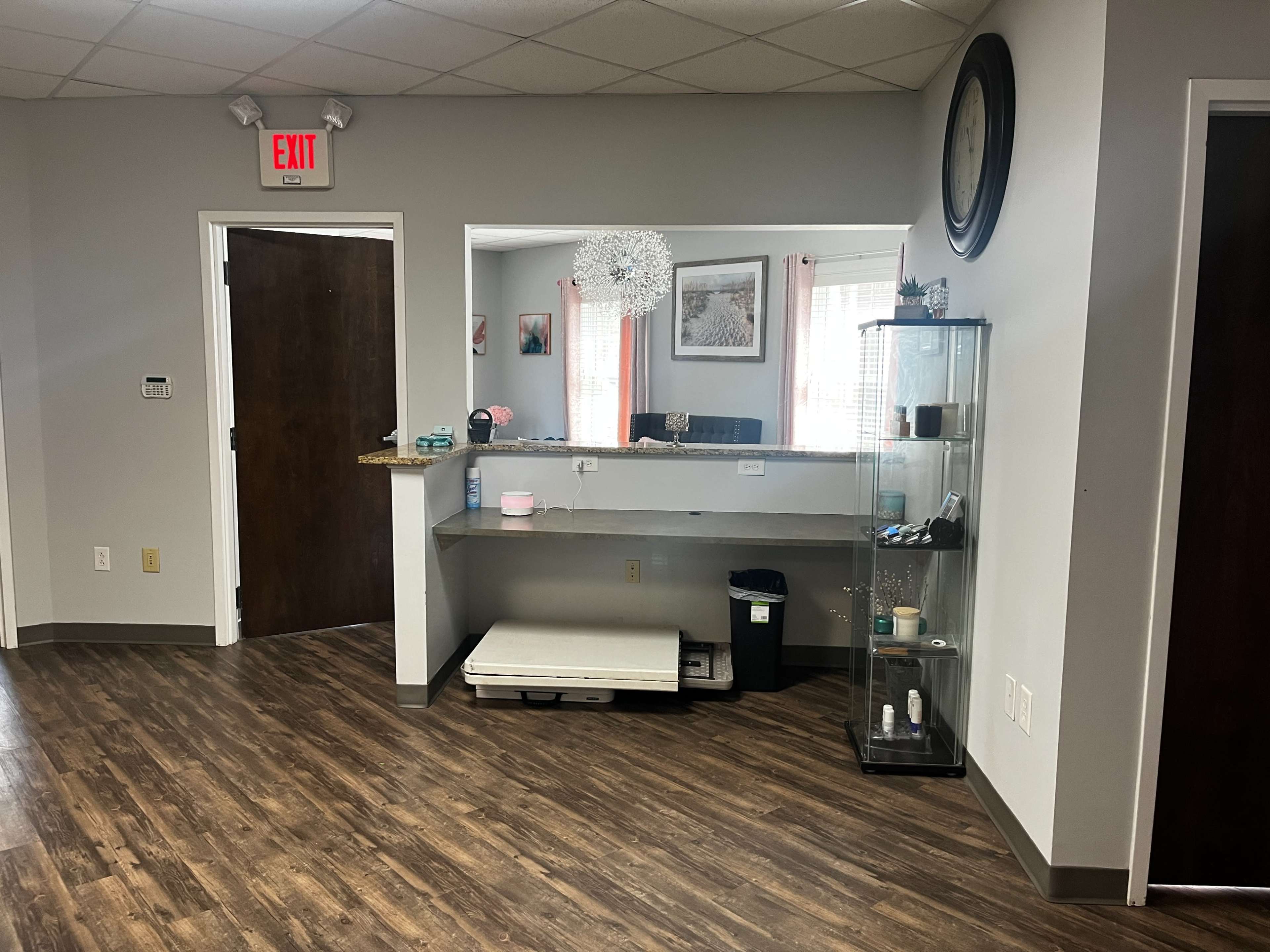 A tidy reception area with a wooden floor, a mirrored counter, and a display case.