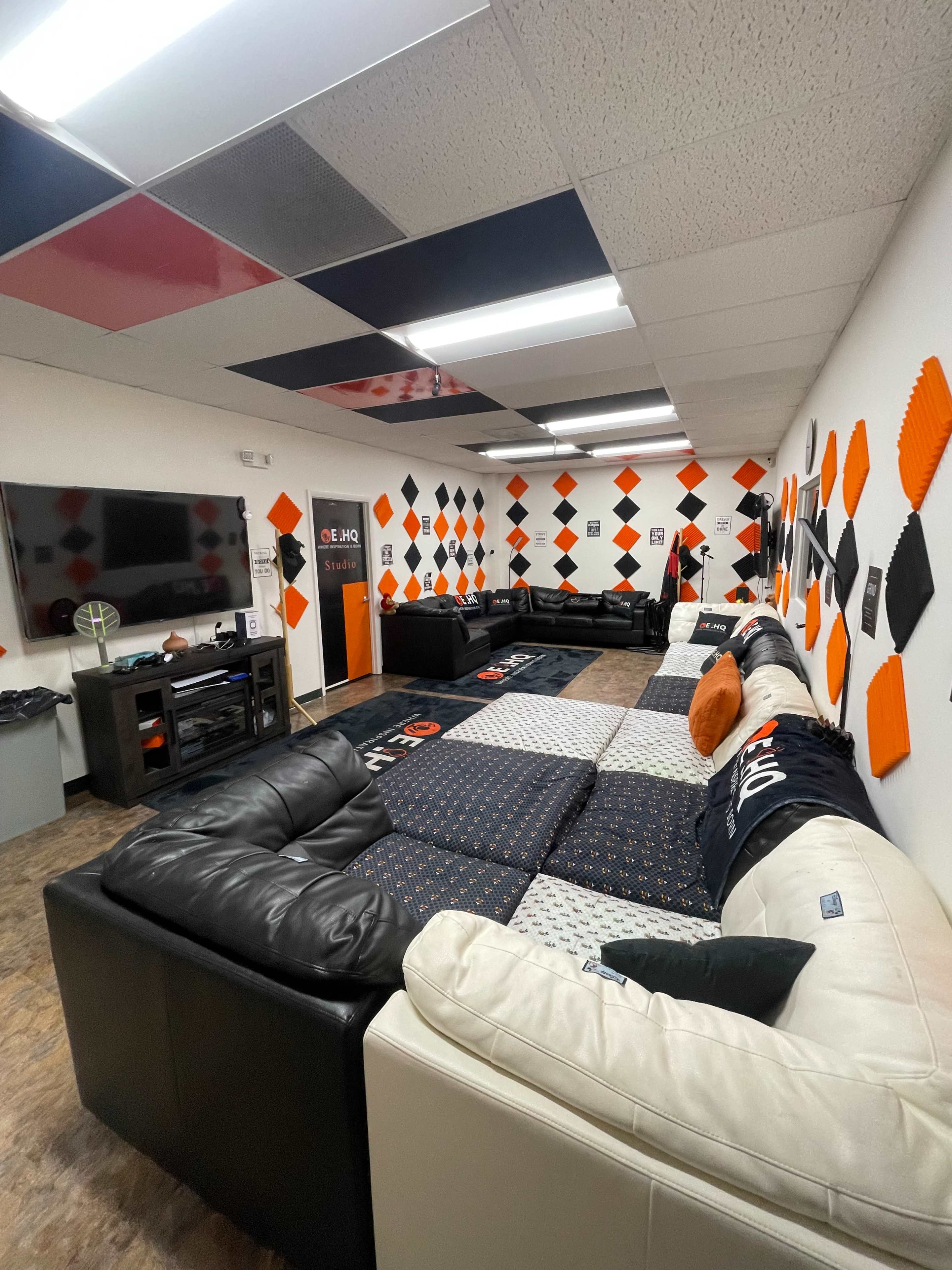 The image shows a lounge area with multiple sectional sofas arranged around a television and decorated walls featuring orange and black geometric patterns.