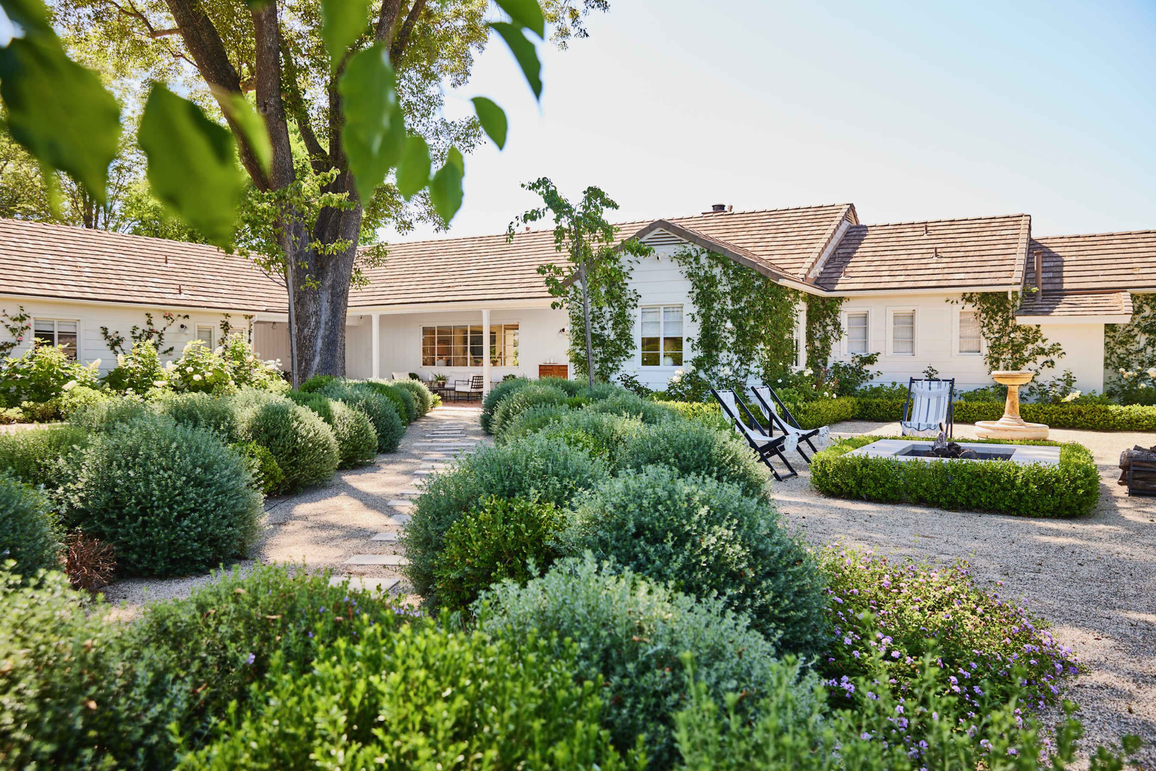 A white, single-story house surrounded by neatly trimmed hedges and gravel pathways.
