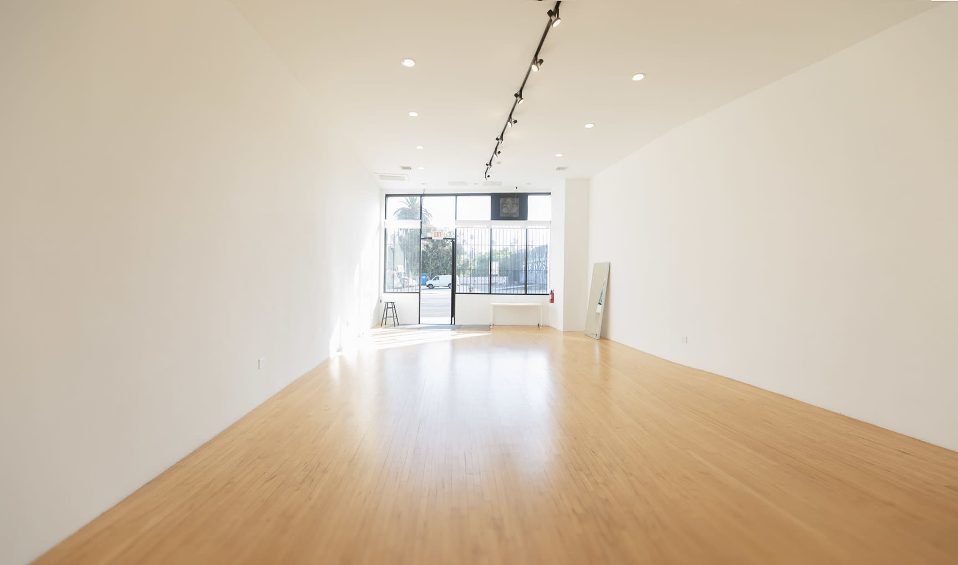 The image shows a spacious, brightly lit interior with bamboo flooring and large windows, revealing a view of an outdoor area.