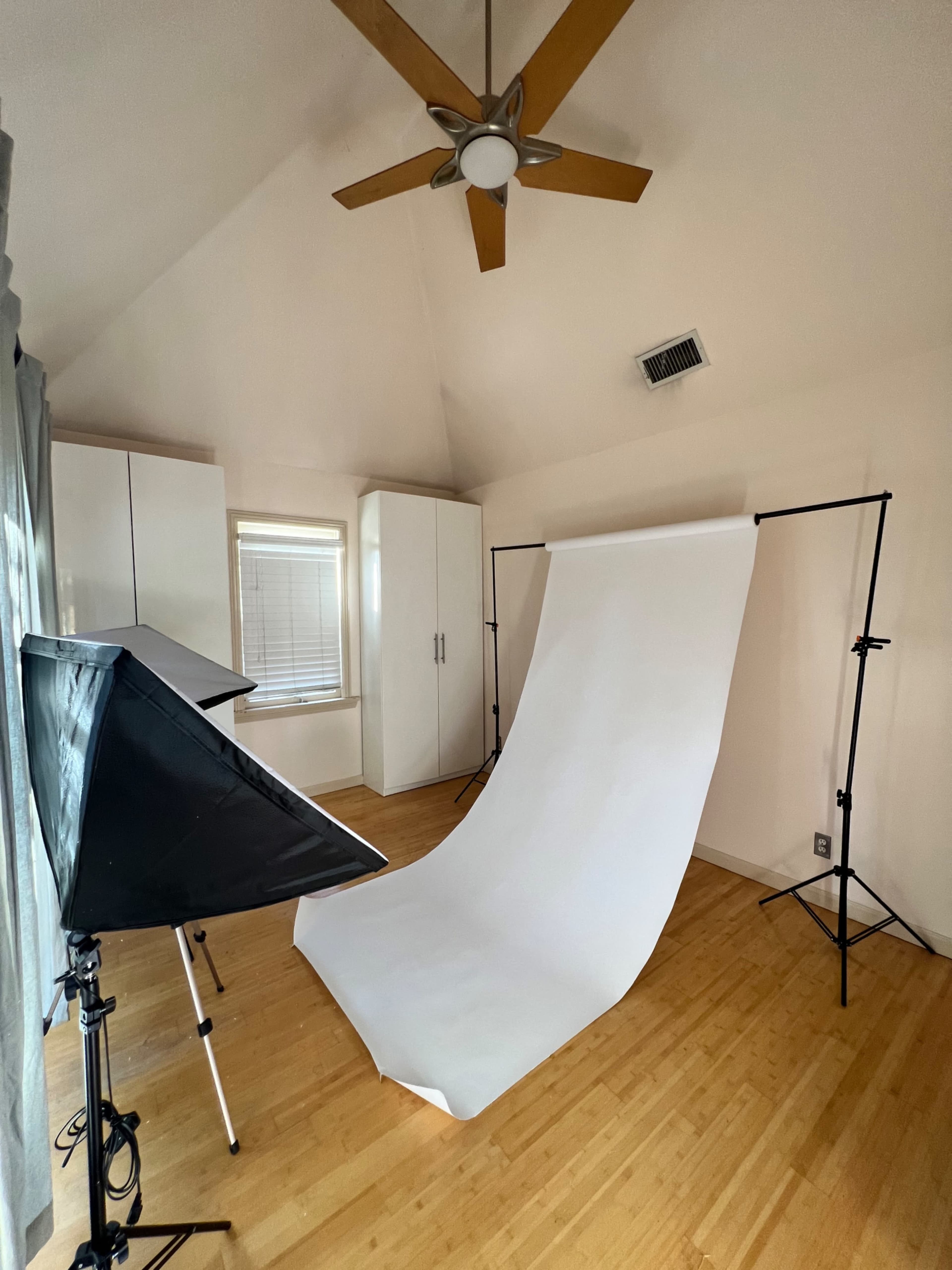 A simple photography setup in a room with a white backdrop, a light source, and a ceiling fan.