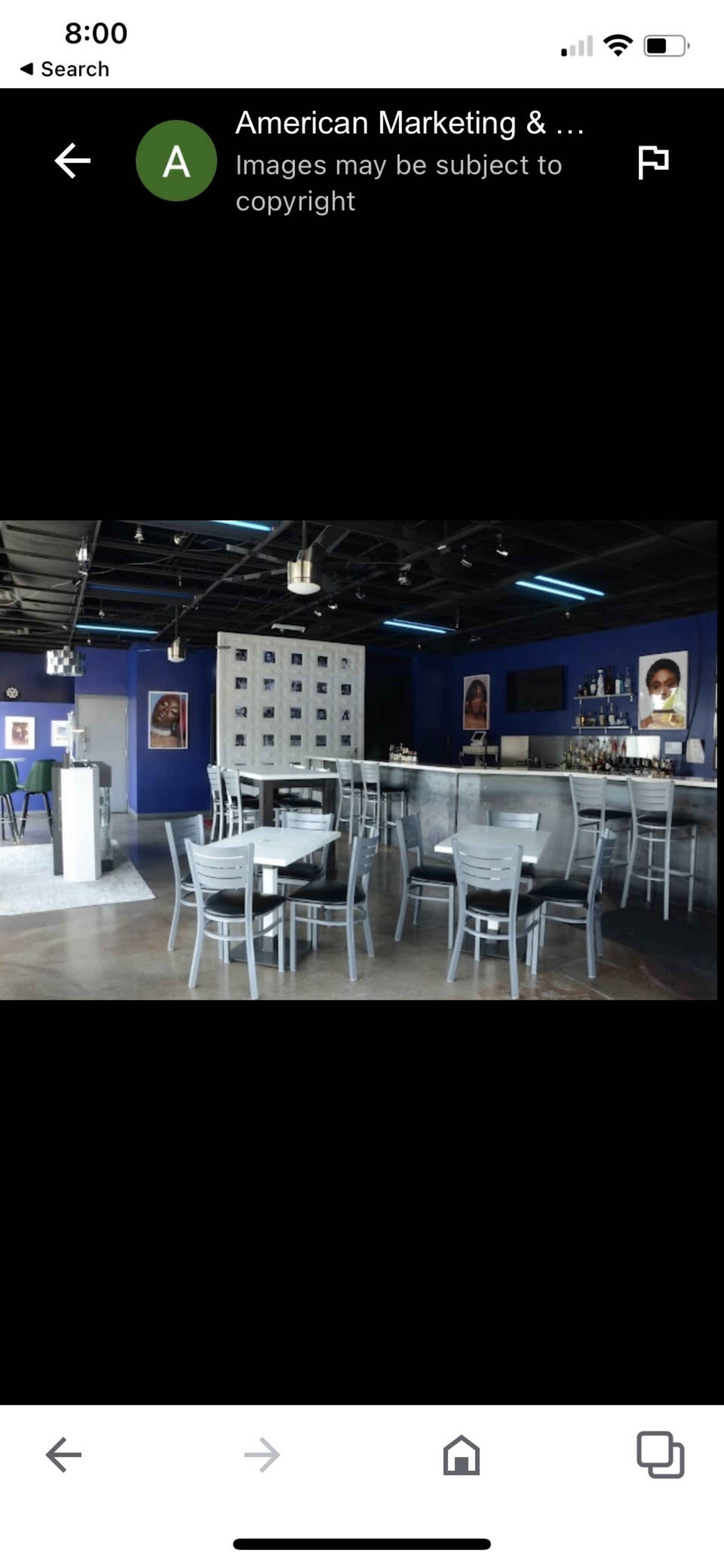 A modern restaurant interior with gray chairs and tables arranged around a bar area in a blue-walled space.