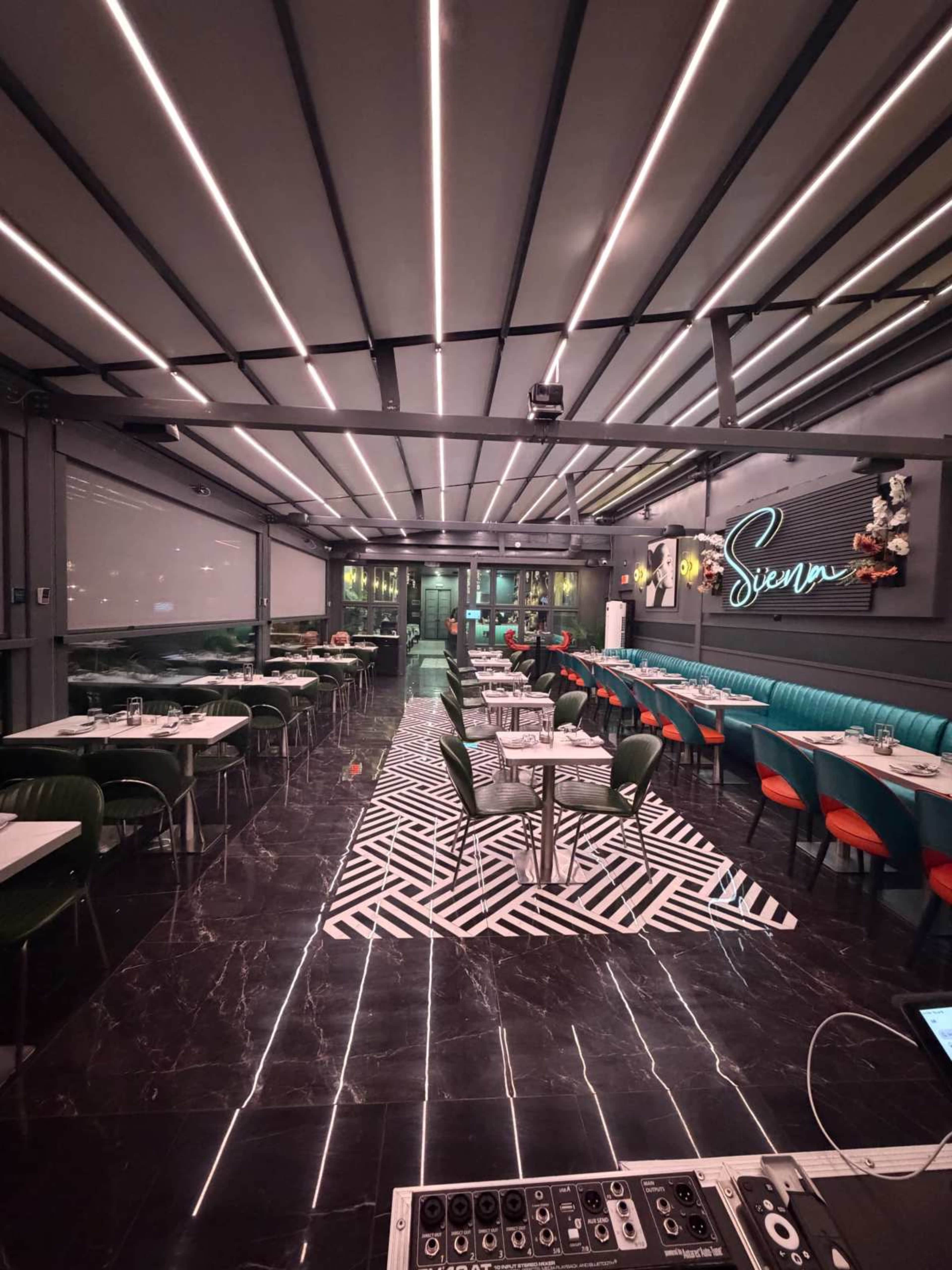 The image shows a modern restaurant interior with striped lighting, black and white flooring, and green and red seating arrangements.