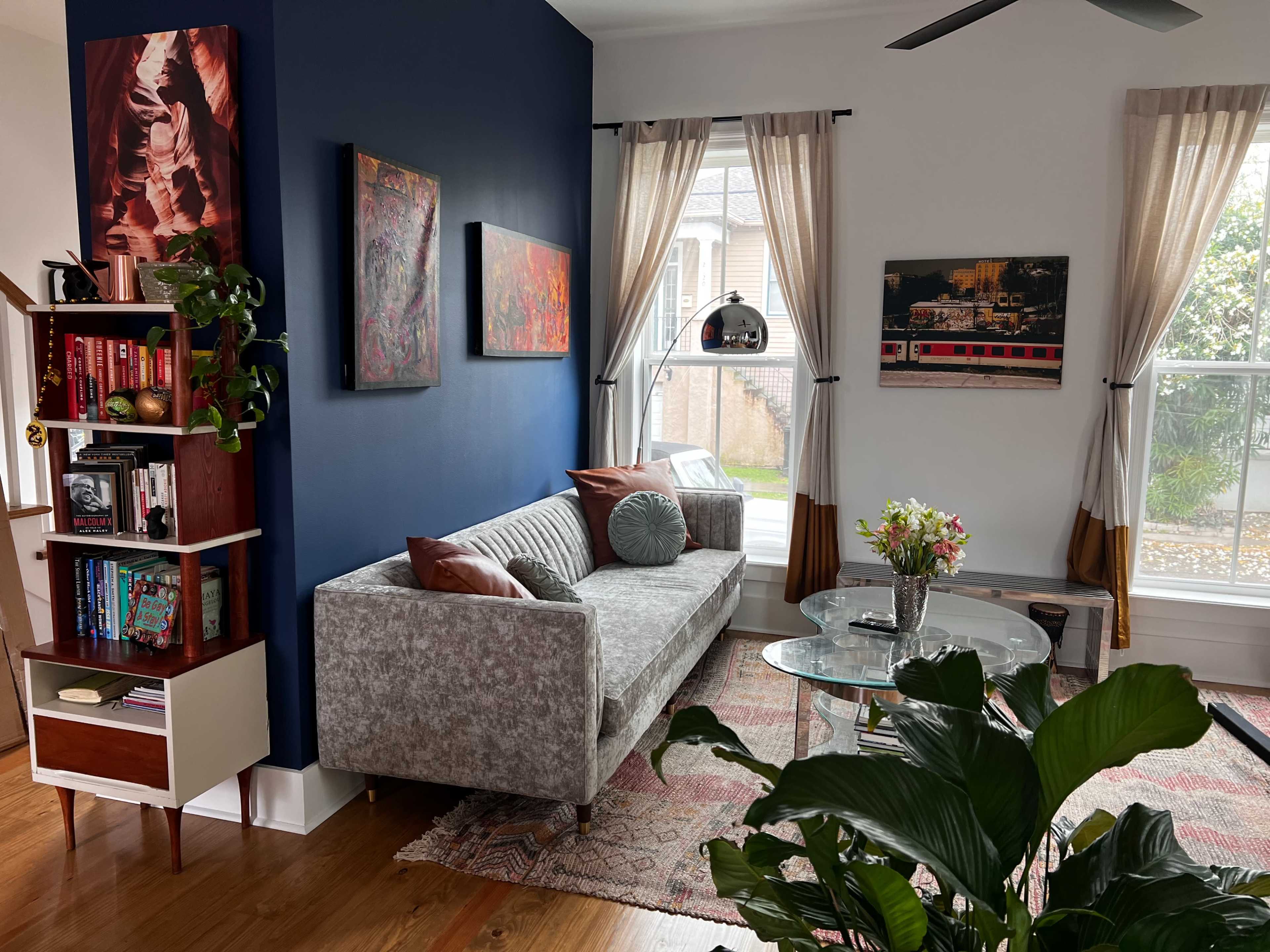 A modern living room with a light gray sofa, a glass coffee table, a bookshelf, and large windows adorned with curtains, creating a cozy atmosphere.