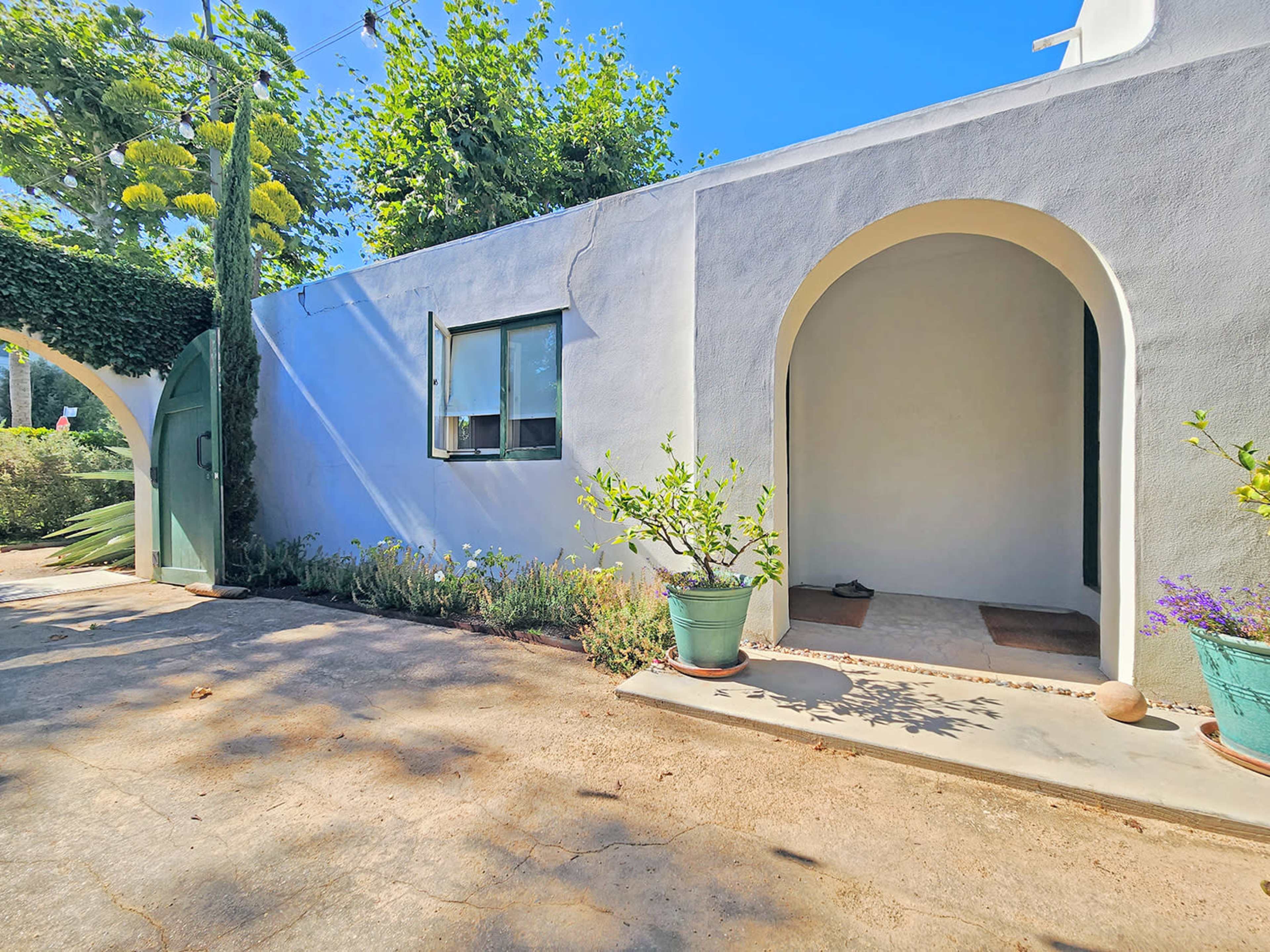 A whitewashed building with arched doorways and a pathway lined with potted plants.