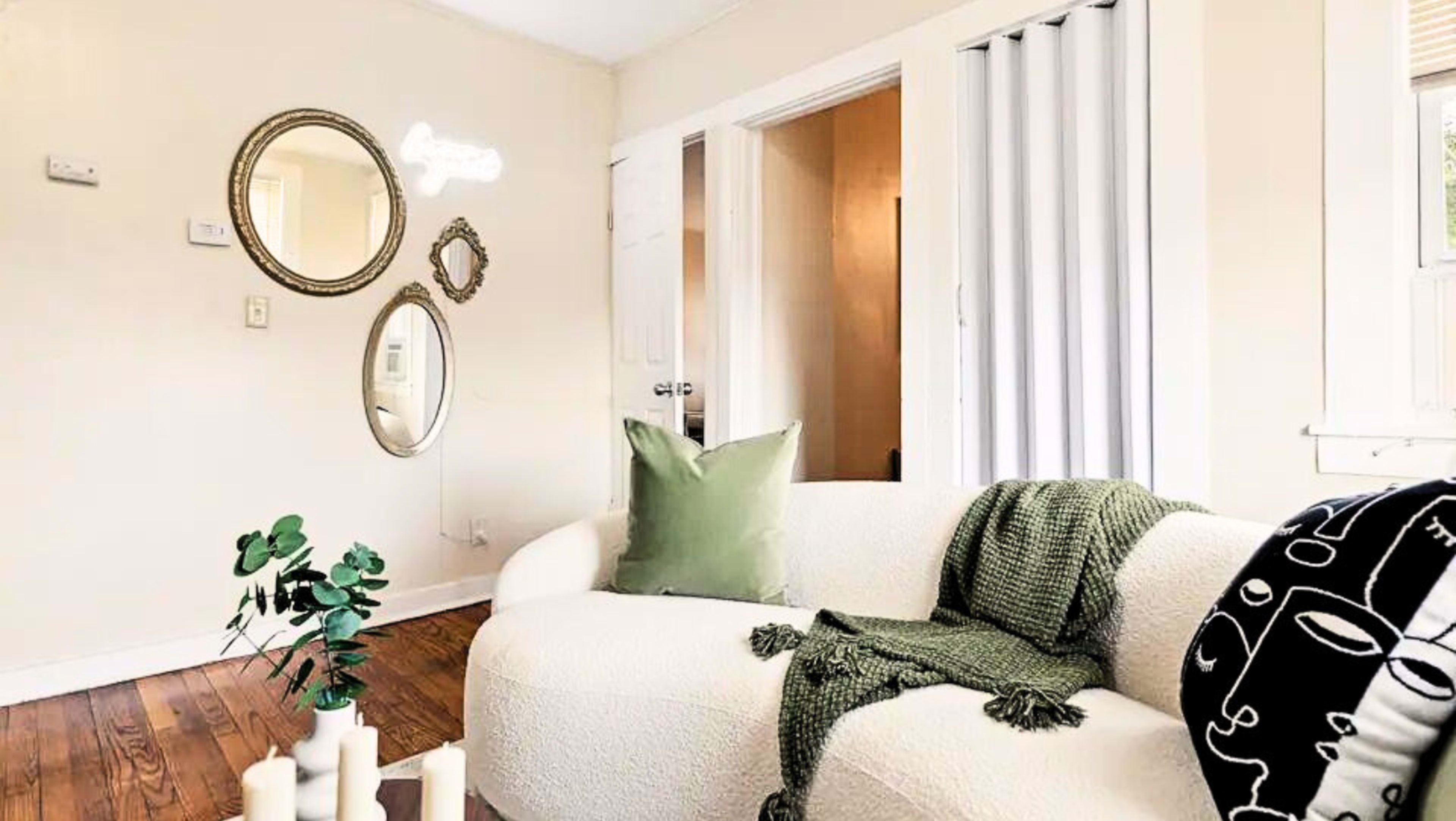 A cozy living room features a white sofa with green accents, surrounded by decorative mirrors and a plant on the floor.