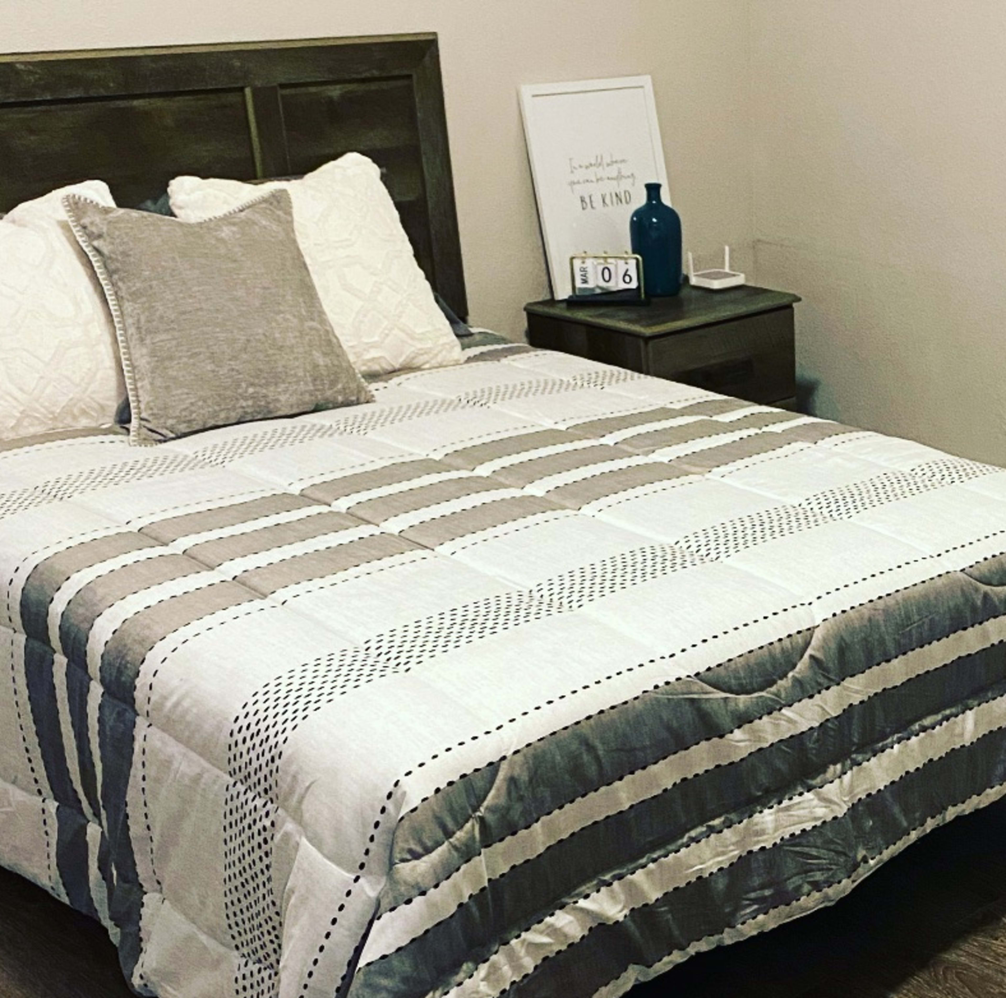A neatly made bed with a patterned quilt is positioned beside a nightstand in a softly lit room.