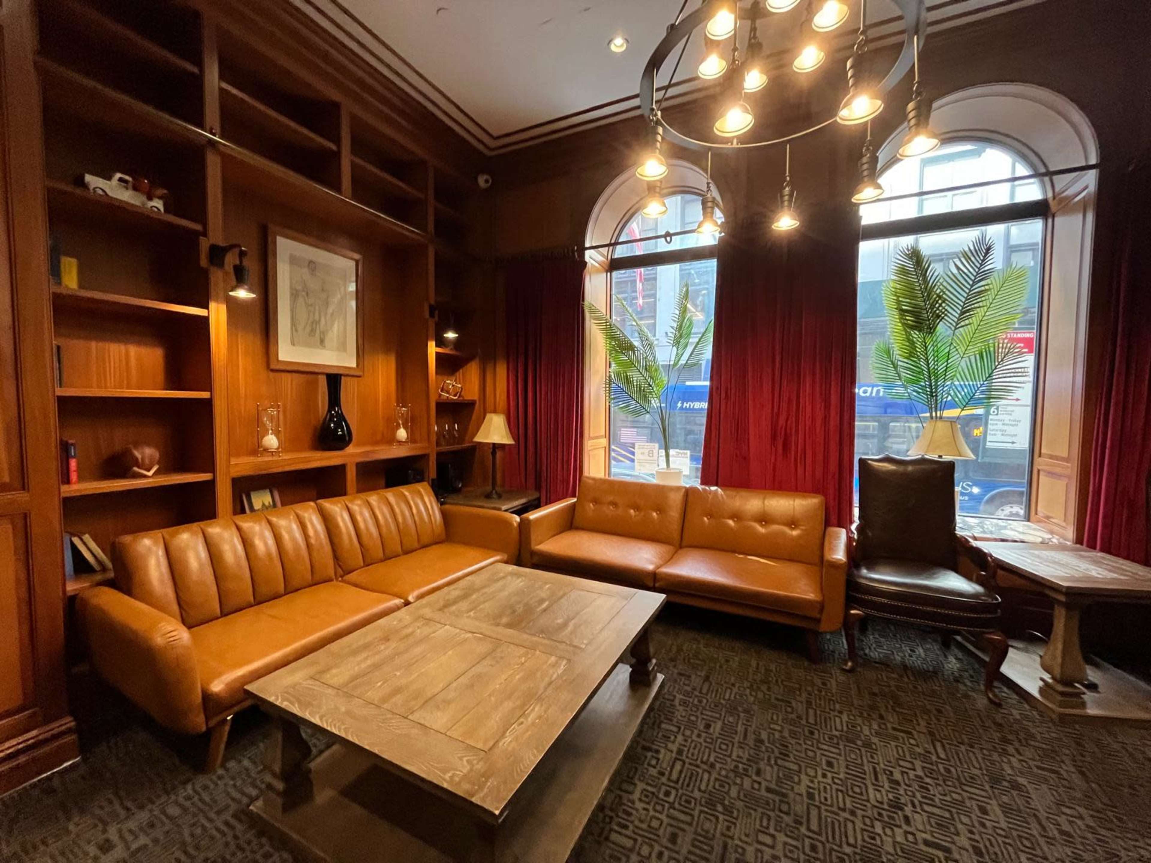 A cozy lounge area with brown leather sofas, a wooden coffee table, and large windows featuring red curtains.
