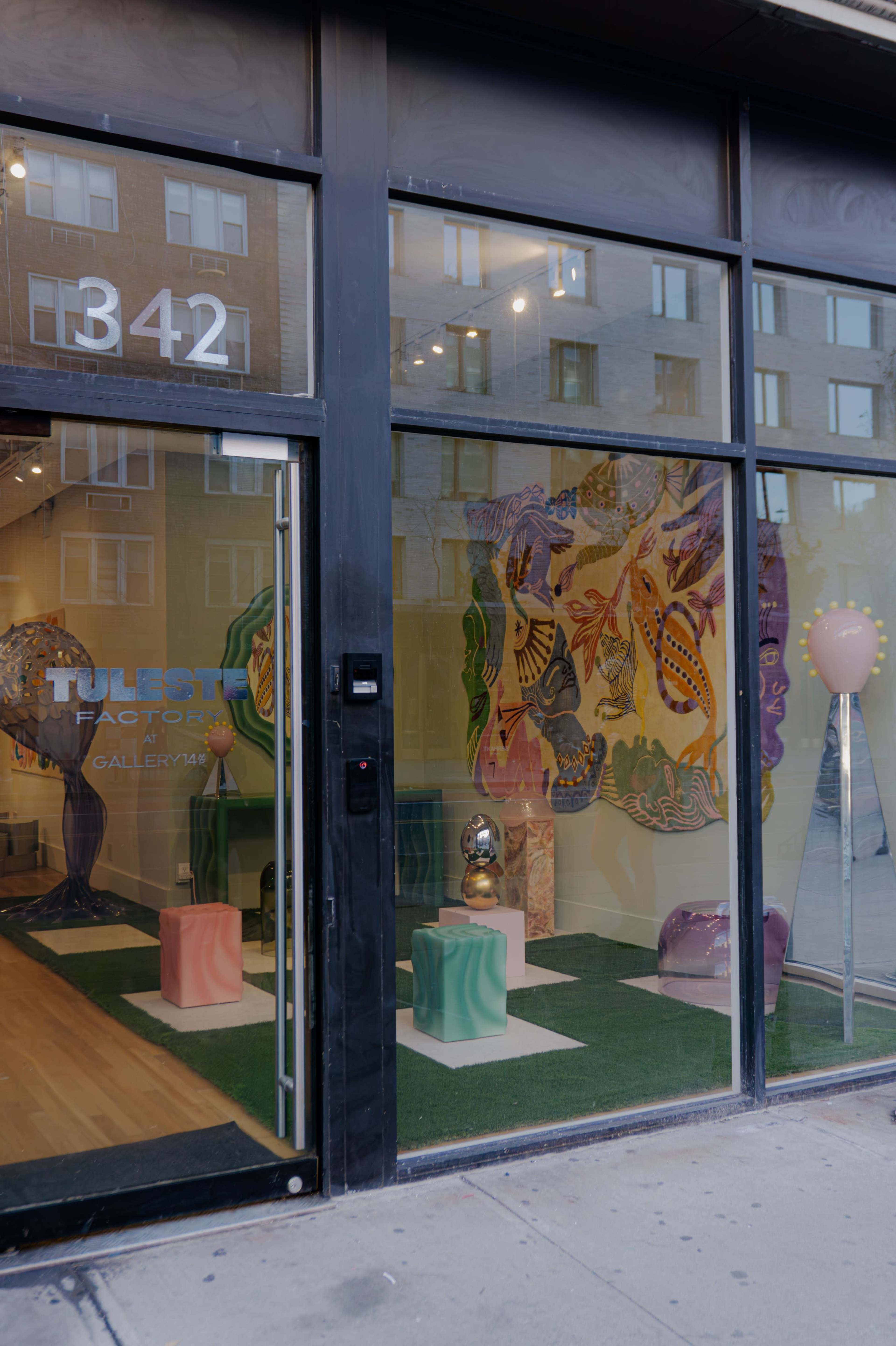 The image shows the exterior of a gallery with large glass windows displaying colorful art and decorative sculptures inside.