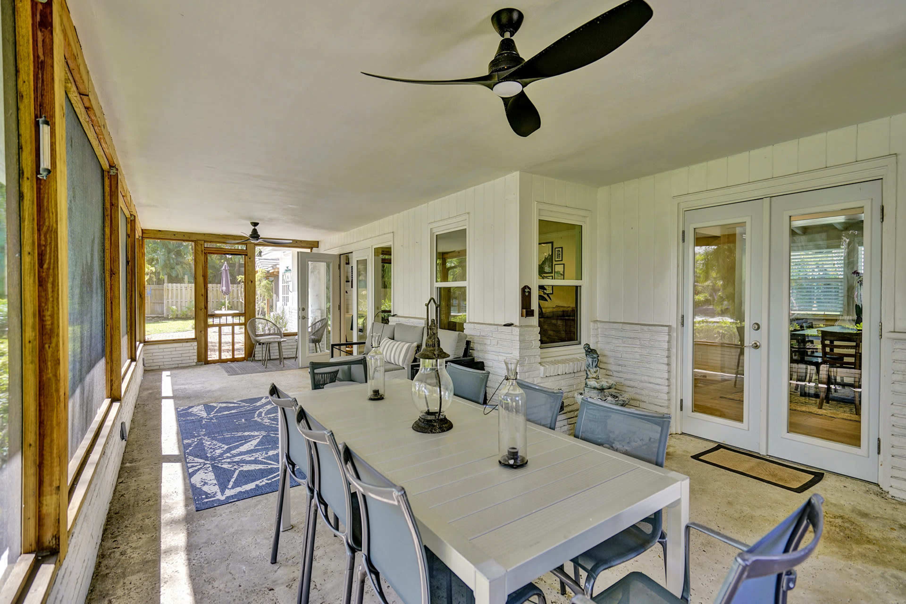 A covered patio area featuring a large dining table surrounded by chairs, a ceiling fan, and glass doors leading to an interior space.