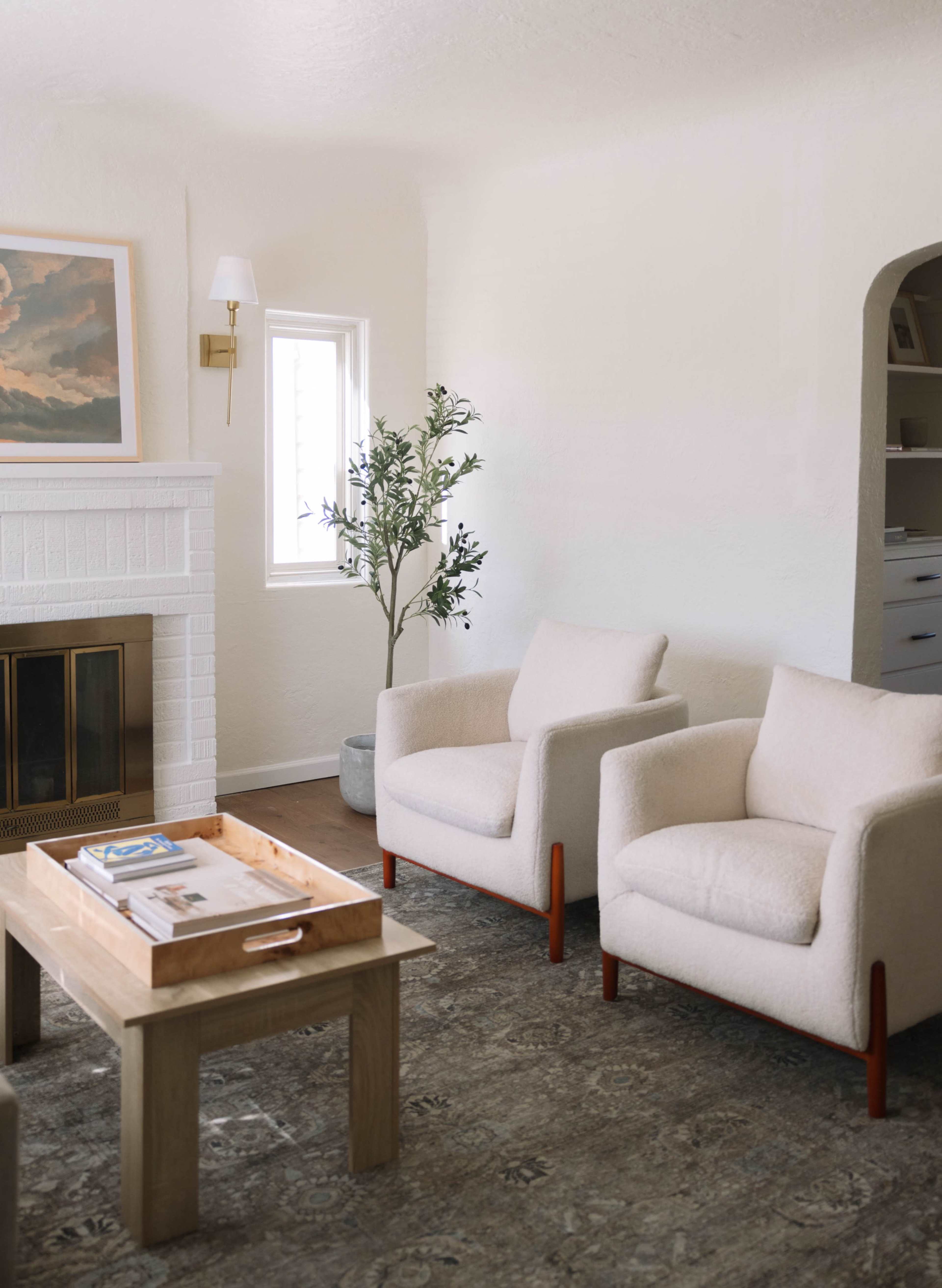 The image shows a cozy living room featuring two upholstered armchairs, a wooden coffee table, and a small indoor plant beside a fireplace.