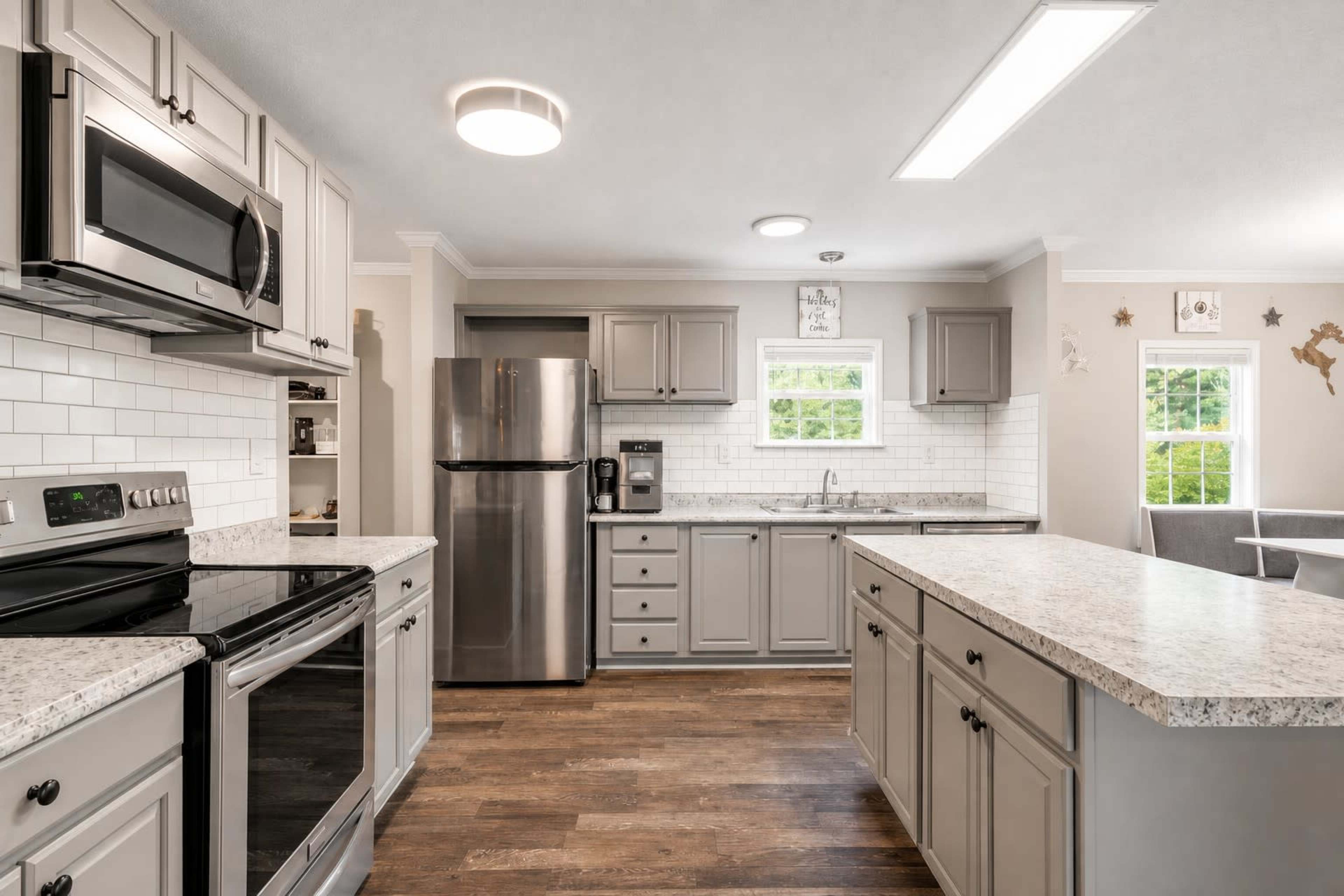 The image shows a modern kitchen with gray cabinetry, stainless steel appliances, and a central island topped with granite.