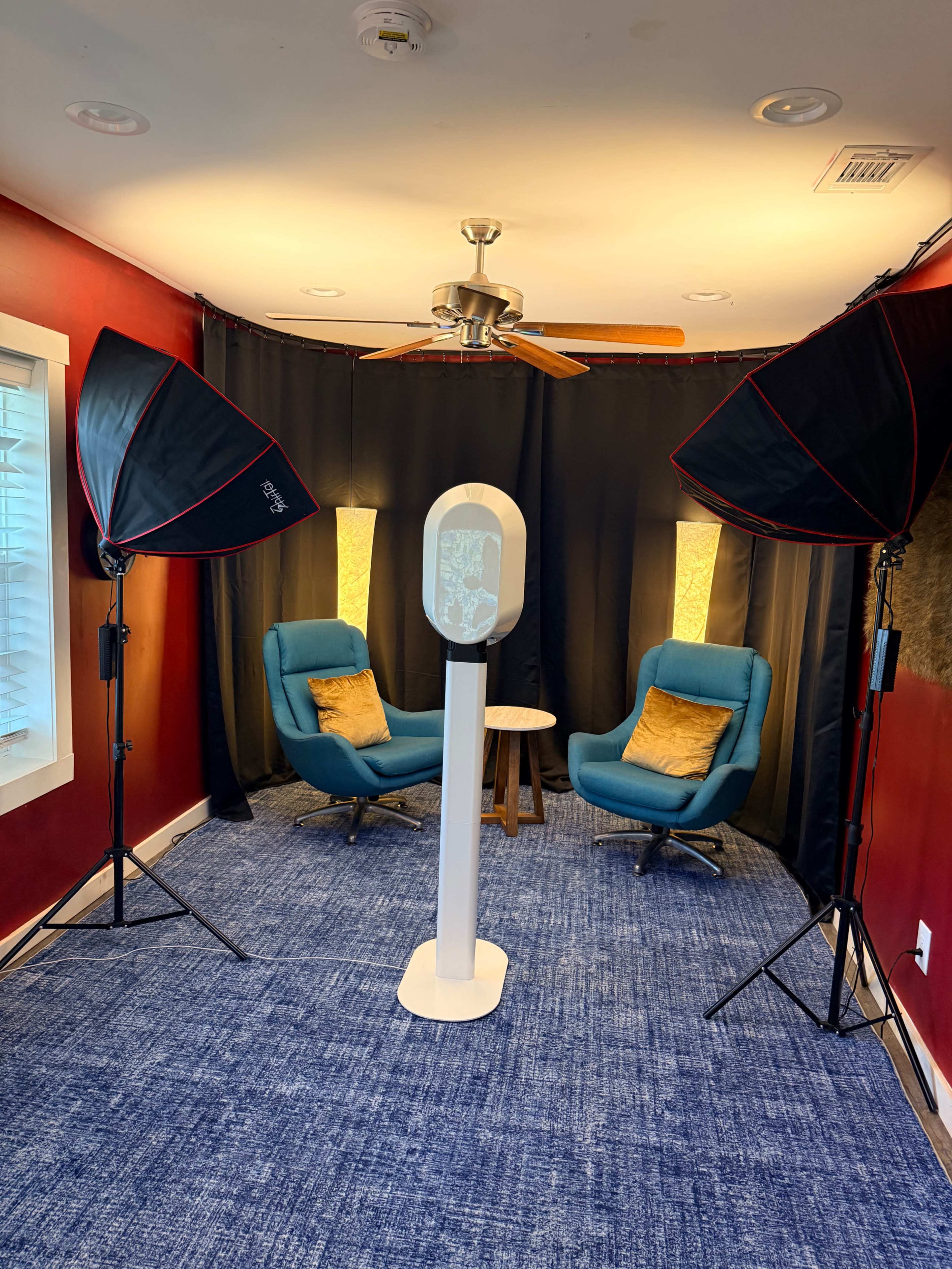 The image shows a small studio setup with two blue chairs, a round table, and softbox lights arranged against a black backdrop.