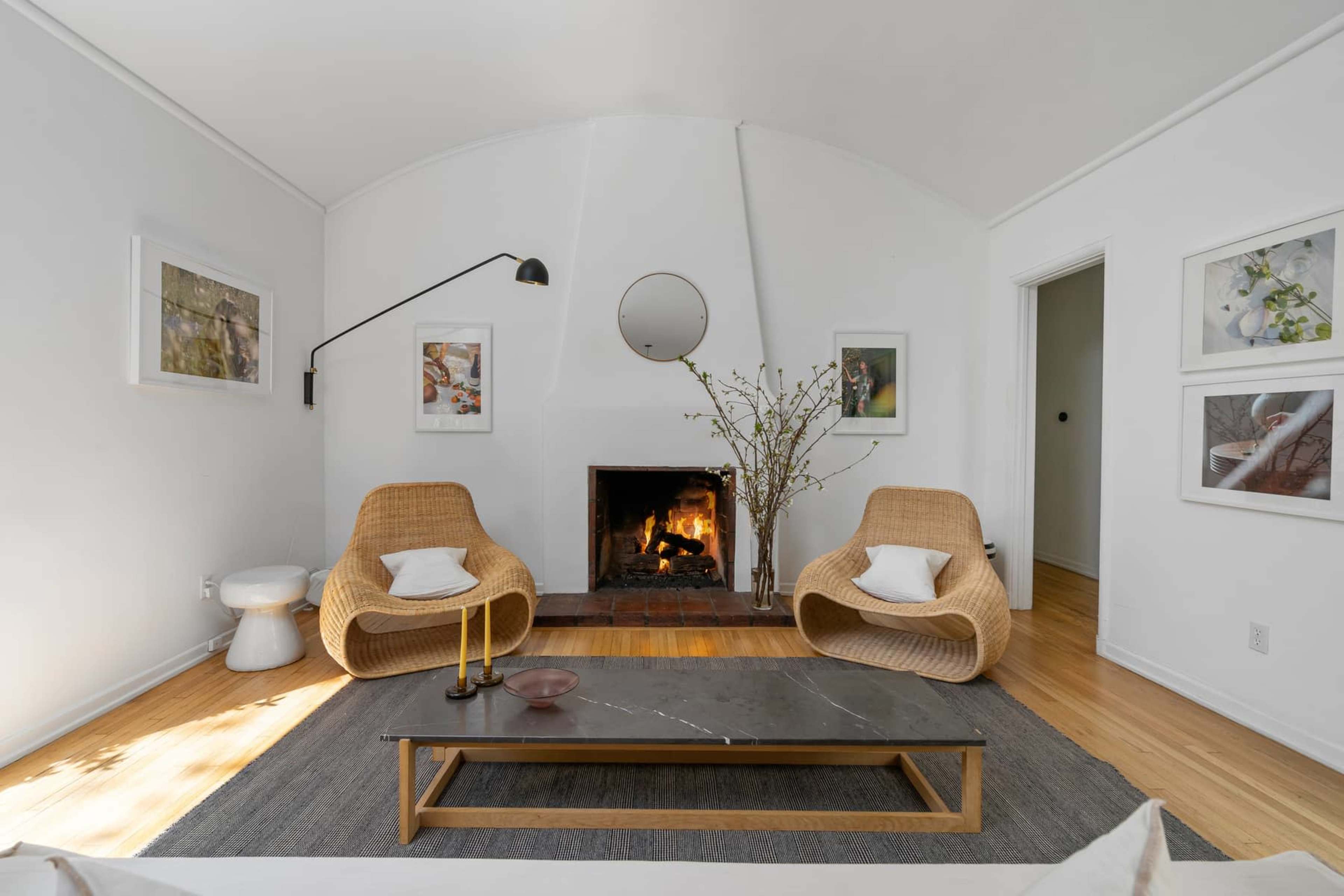A living room features a fireplace surrounded by two wicker chairs, a coffee table, and framed art on the walls.