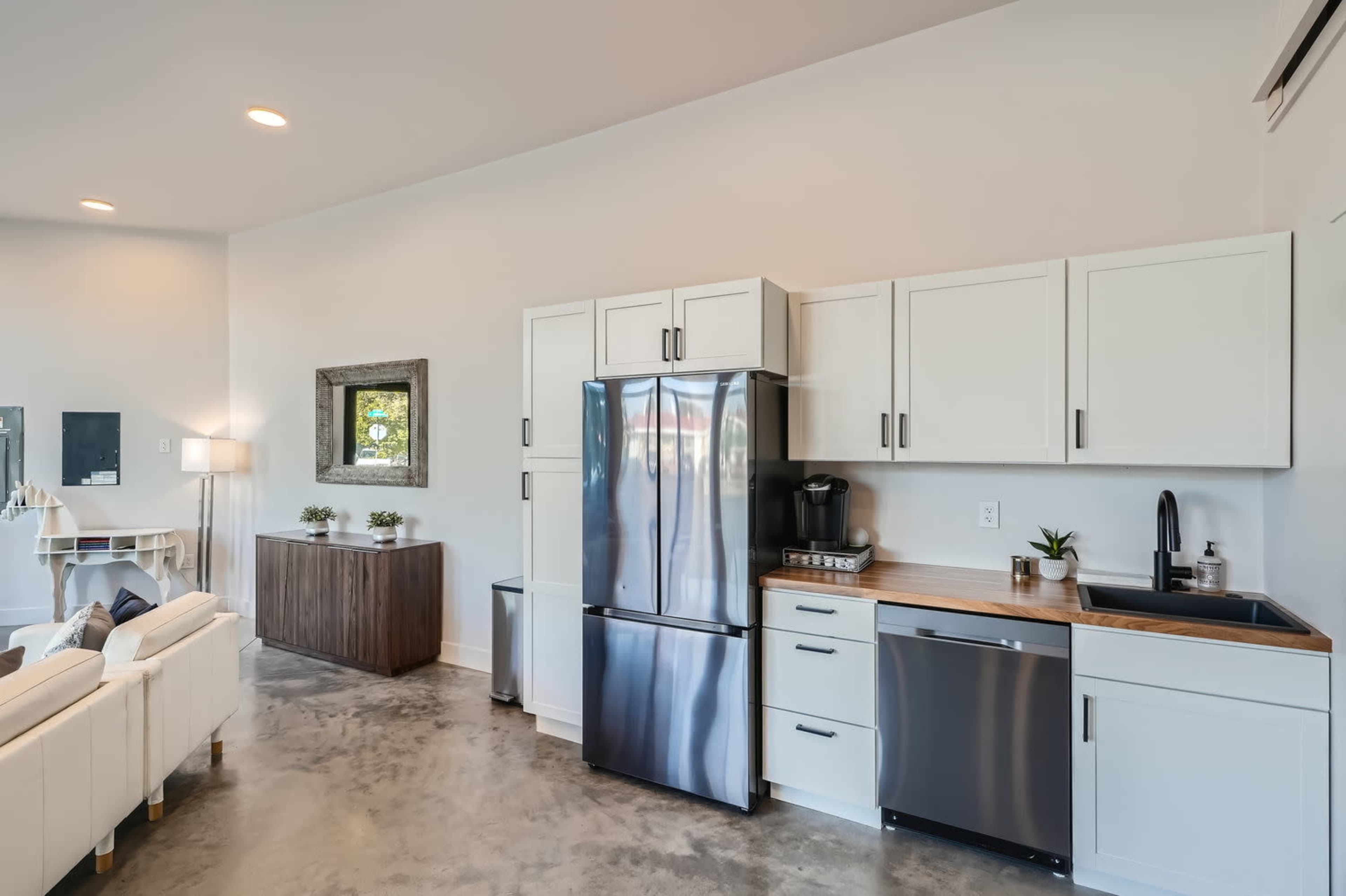 The image shows a modern kitchen area featuring white cabinets, stainless steel appliances, and a wood countertop.