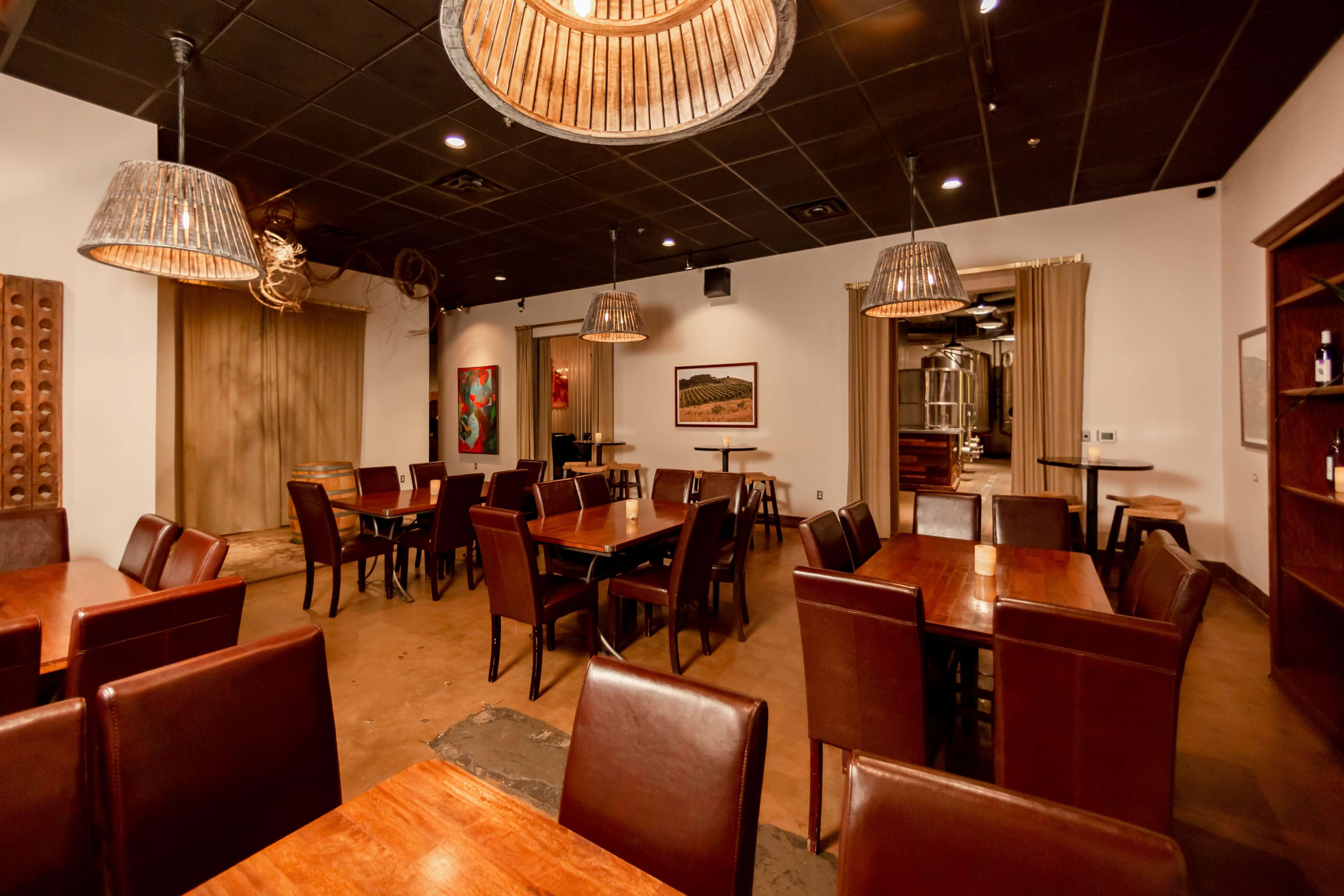 A spacious restaurant interior with wooden tables and chairs, woven pendant lights, and artwork on the walls.