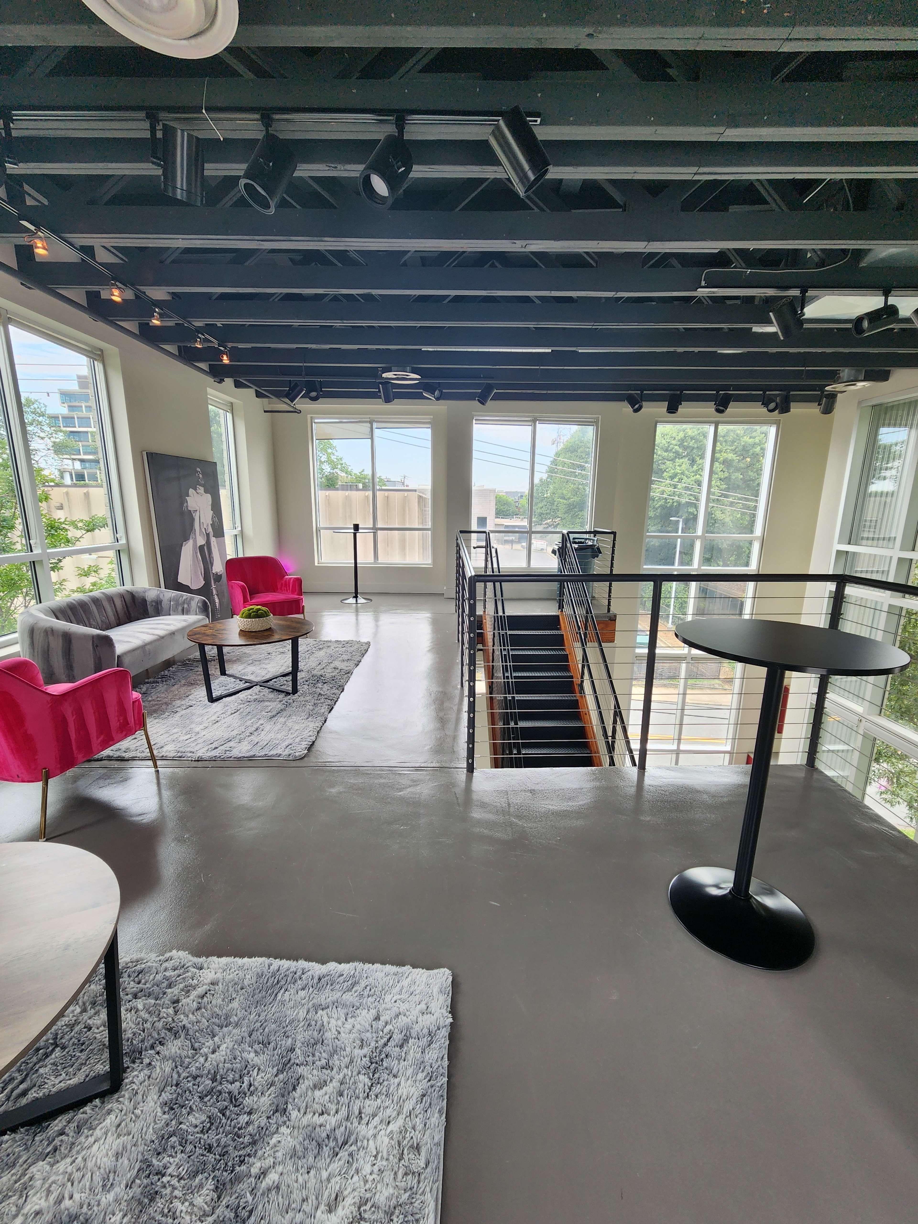 A large, well-lit room with modern furniture, including pink chairs, a coffee table, and a staircase leading to a lower level.