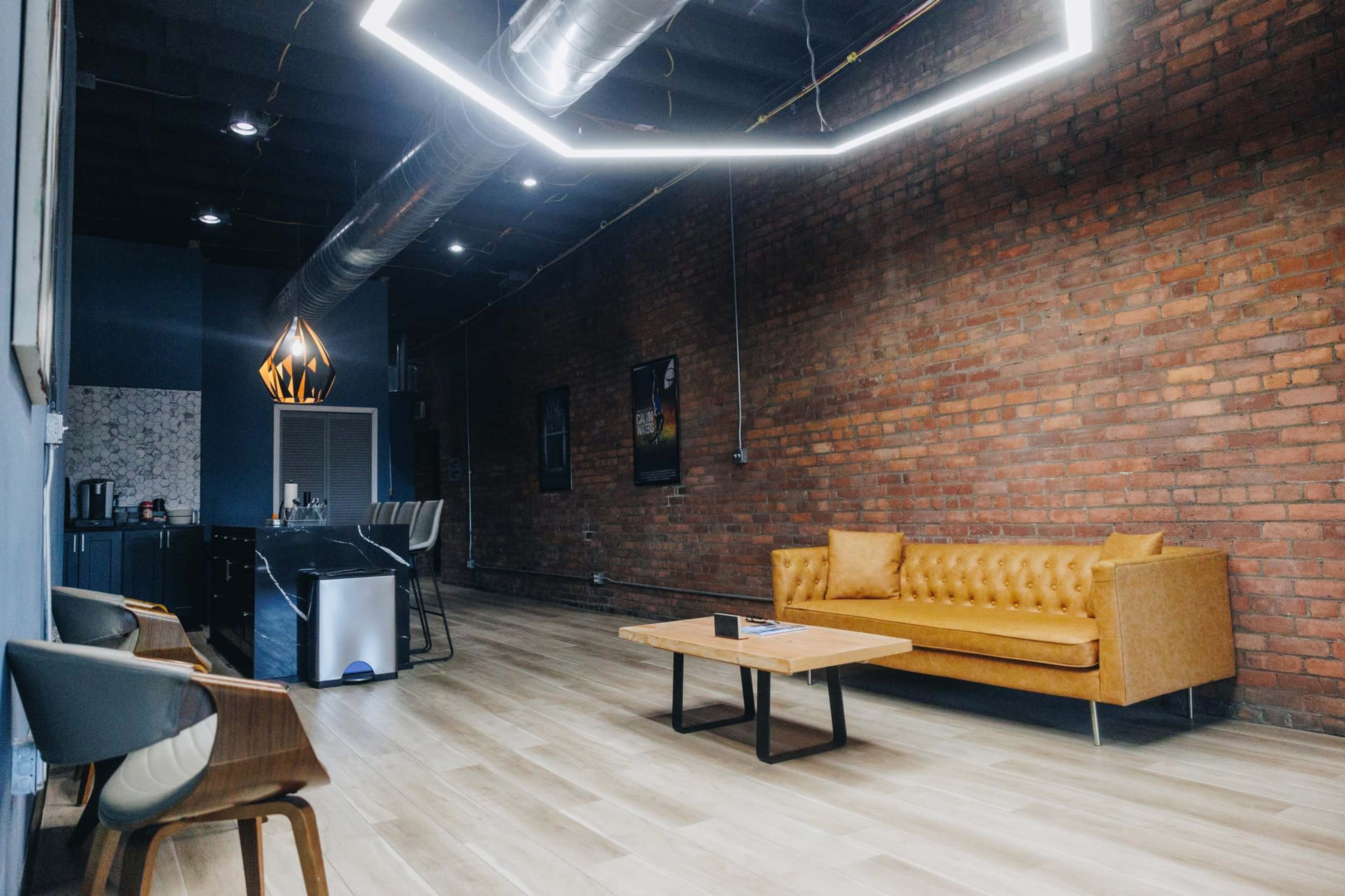 The image shows a modern interior space with a brick wall, wooden floors, a leather sofa, and a countertop with seating.
