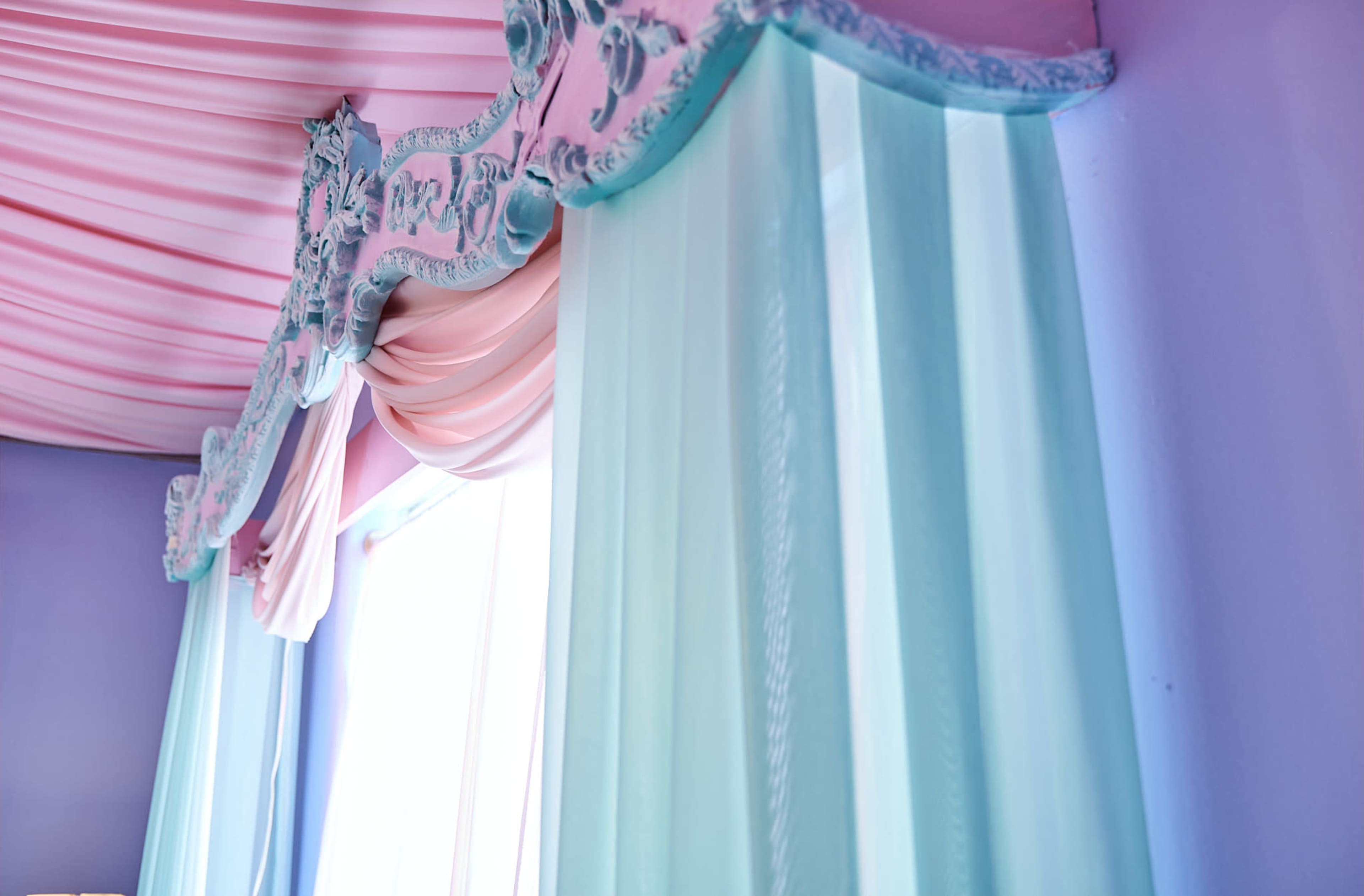 A corner of a room with pastel-colored drapery and ornate valance above a window.