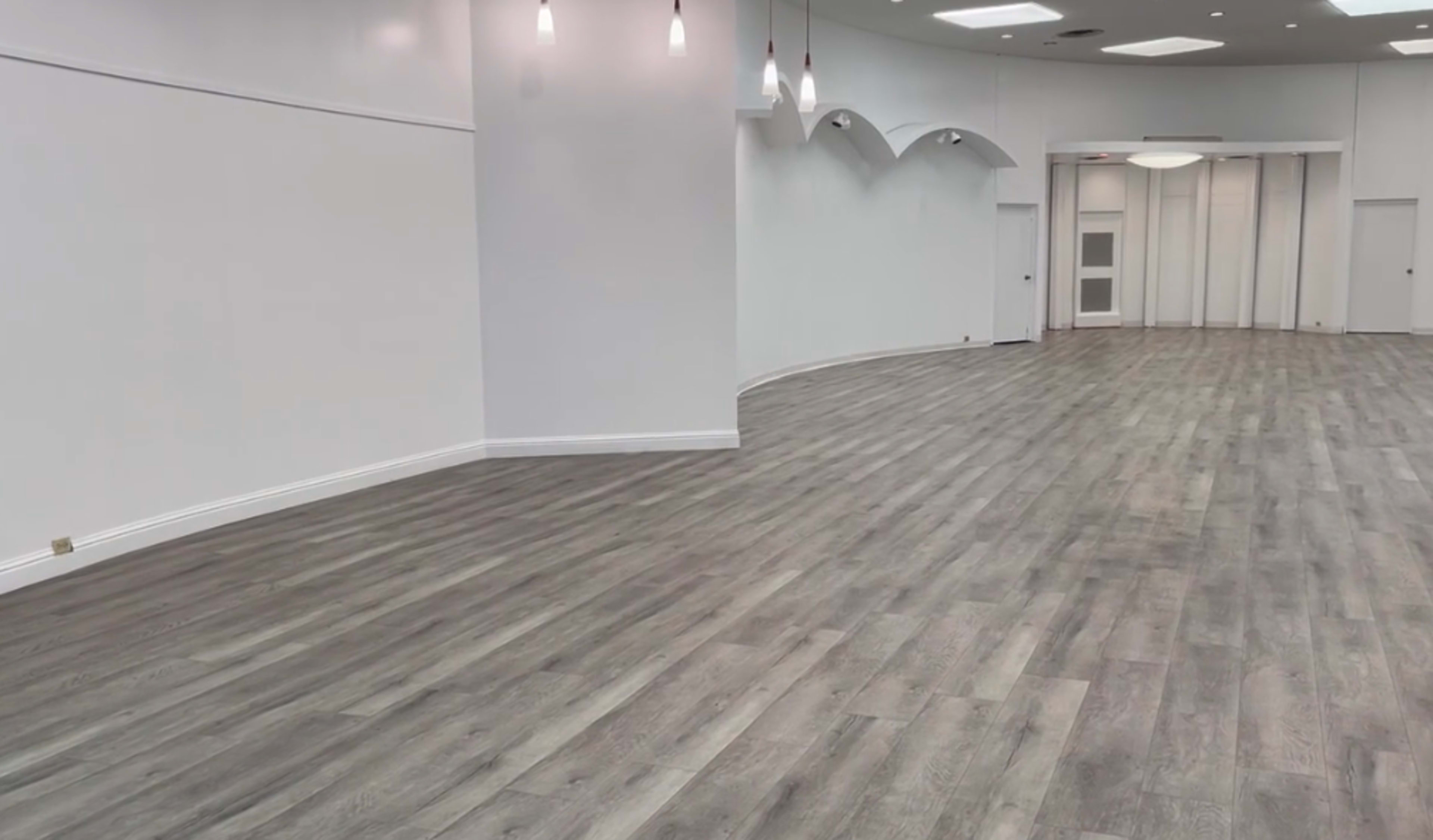An empty interior space with white walls and a wooden floor, featuring recessed lighting and a curved design.