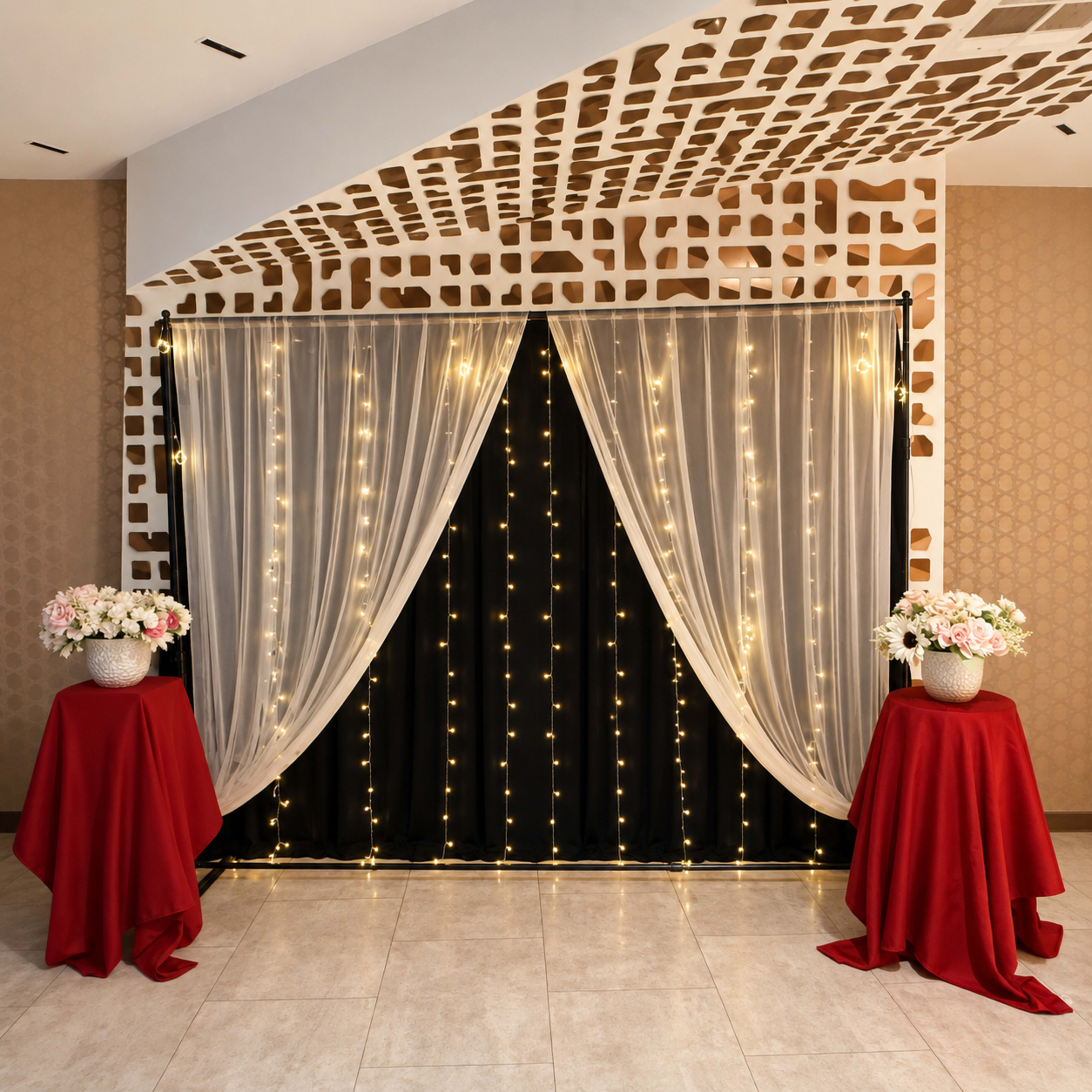 The image shows a decorative backdrop with curtains and string lights, flanked by two tables covered in red tablecloths with floral arrangements.
