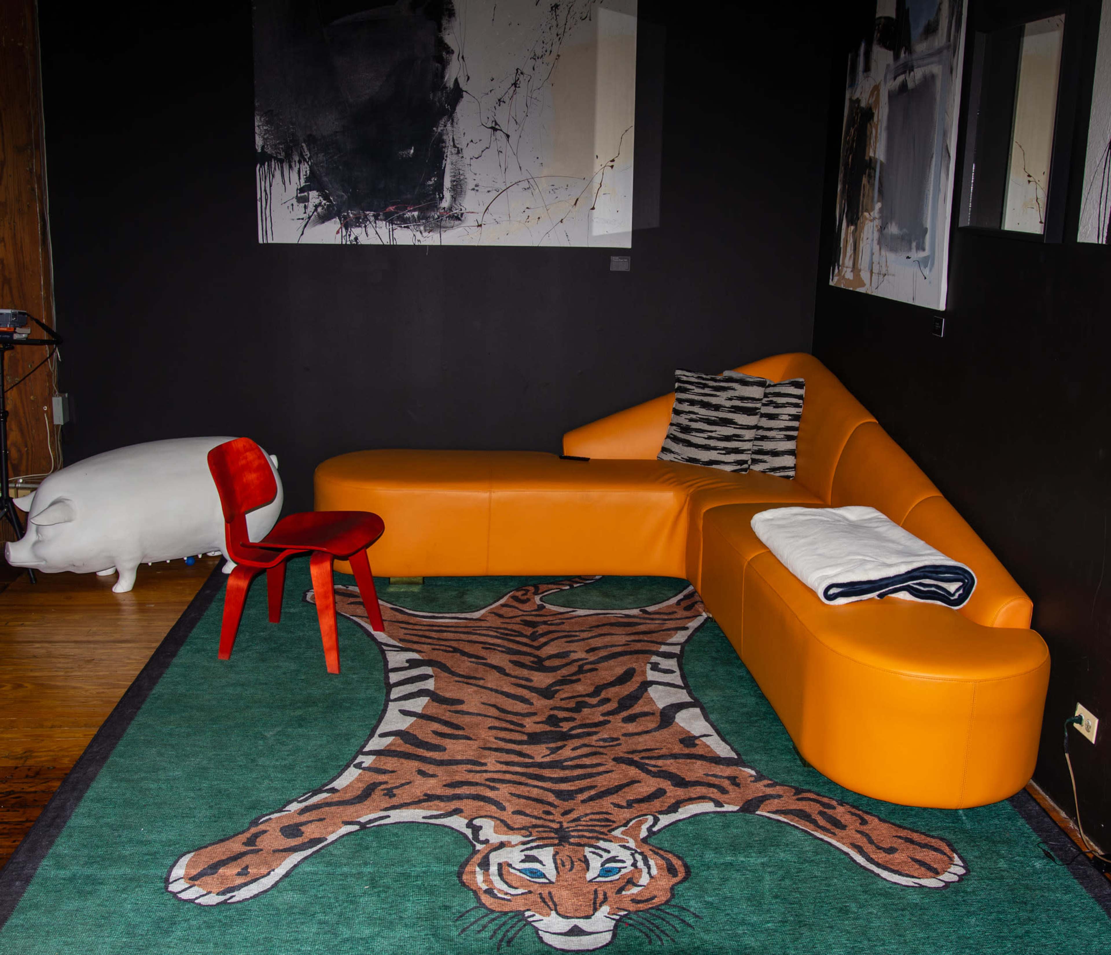 A modern living room featuring an orange sectional sofa, a red chair, and a rug with a tiger print on a wooden floor.