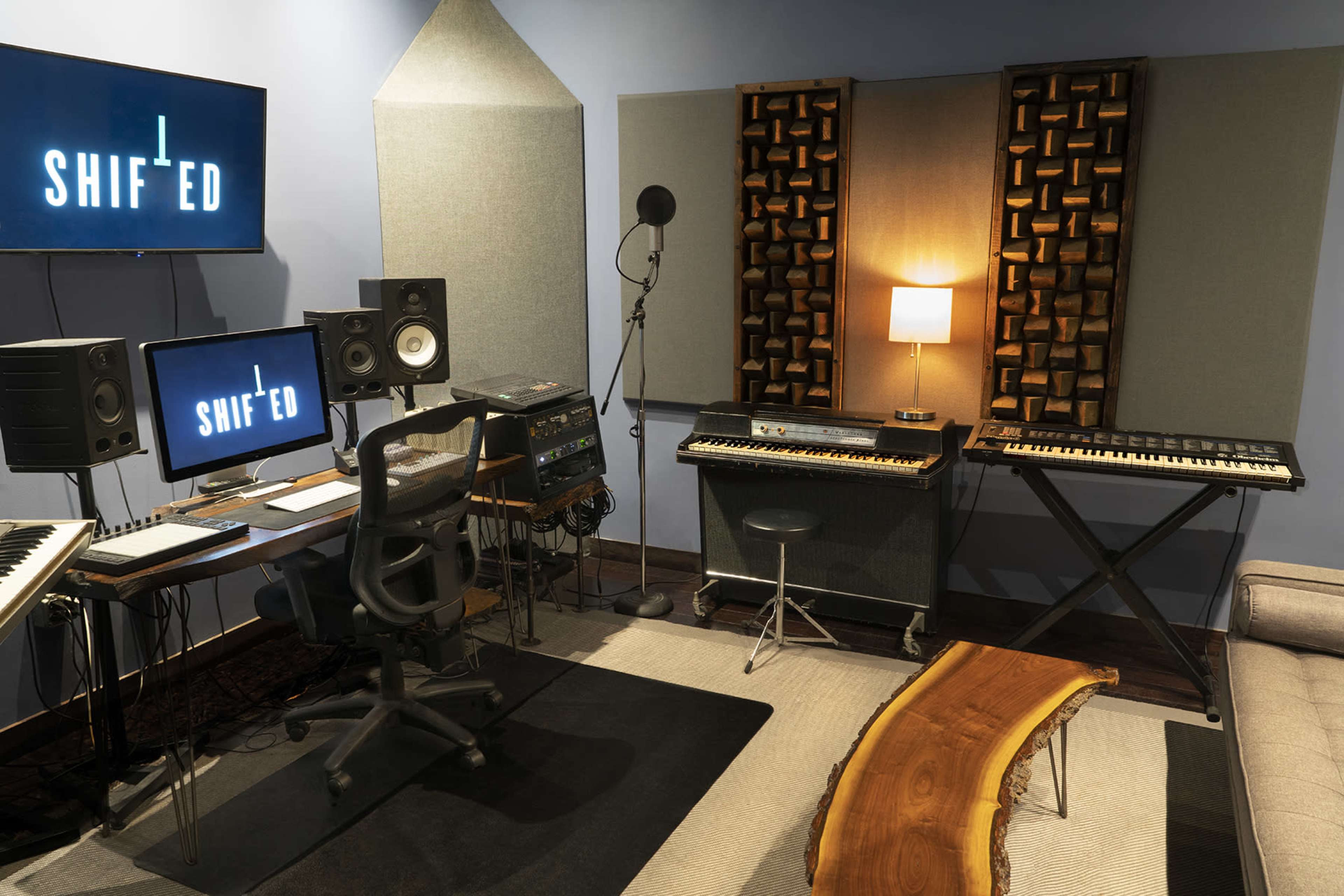 The image shows a music studio equipped with computer workstations, speakers, a microphone, and a keyboard, featuring a modern design.