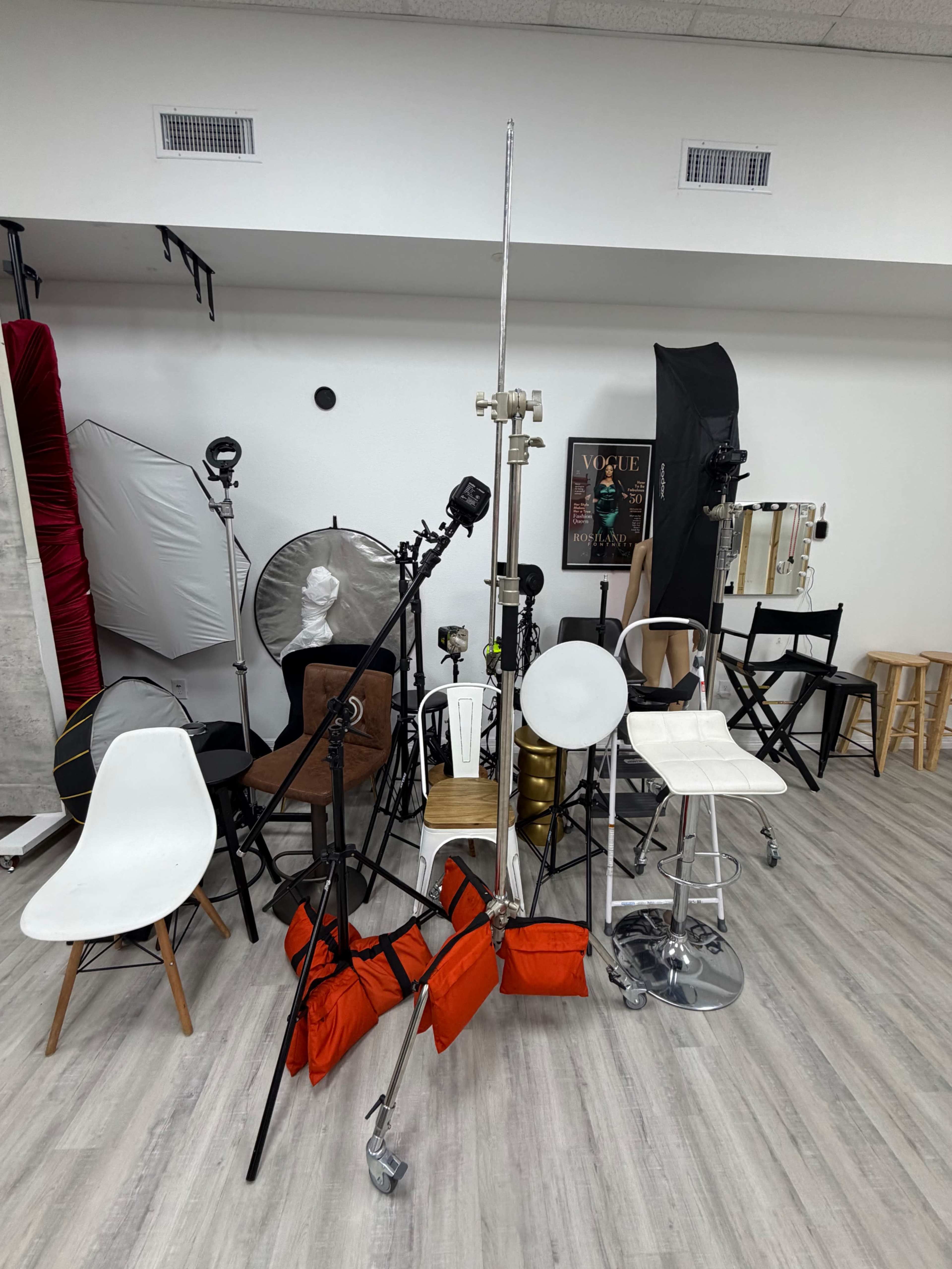 The image shows a studio setup with various lighting equipment, backdrops, and chairs arranged in a photography workspace.