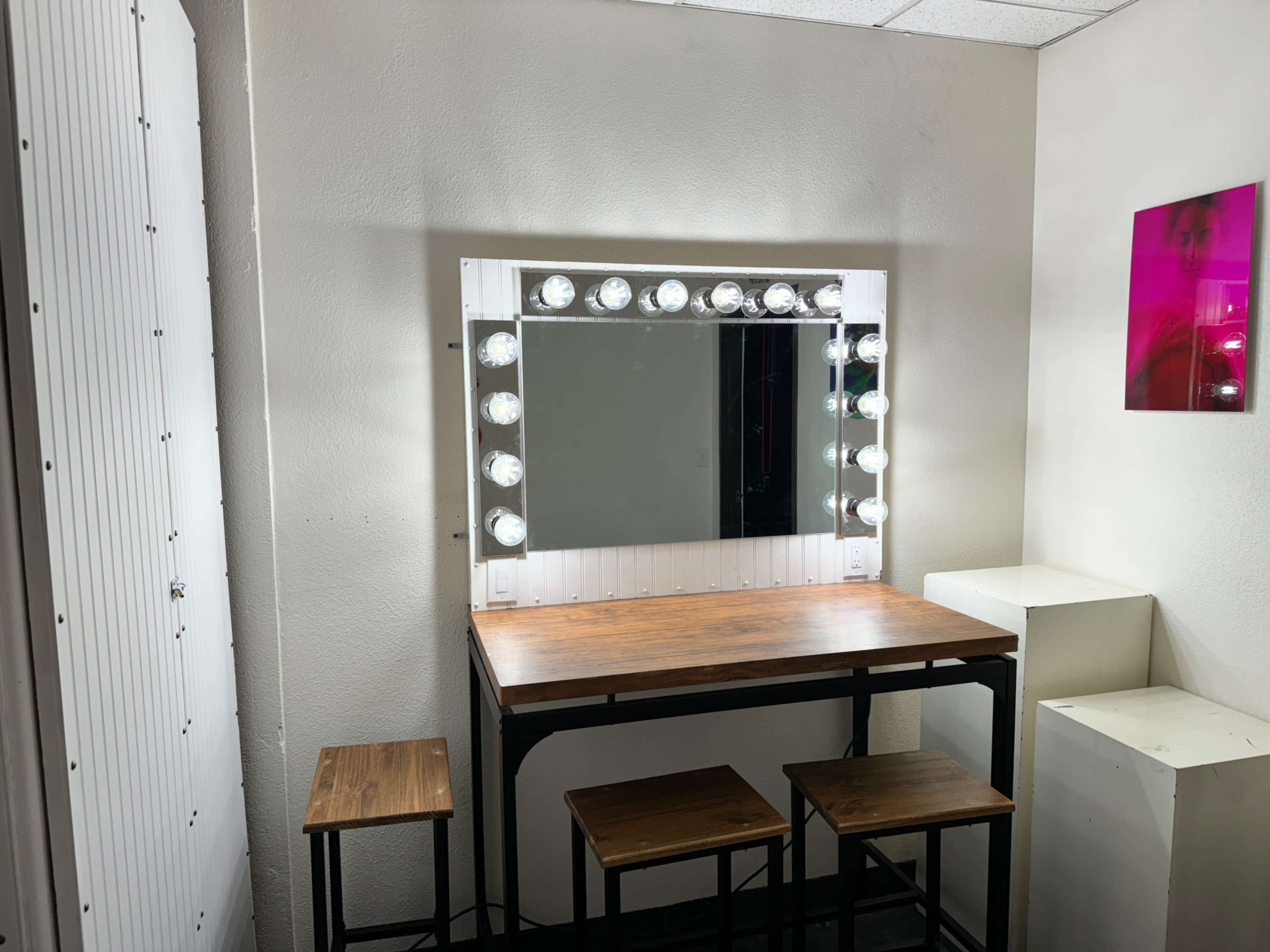 The image shows a well-lit vanity mirror with a wooden table and two matching stools in a minimalist room.