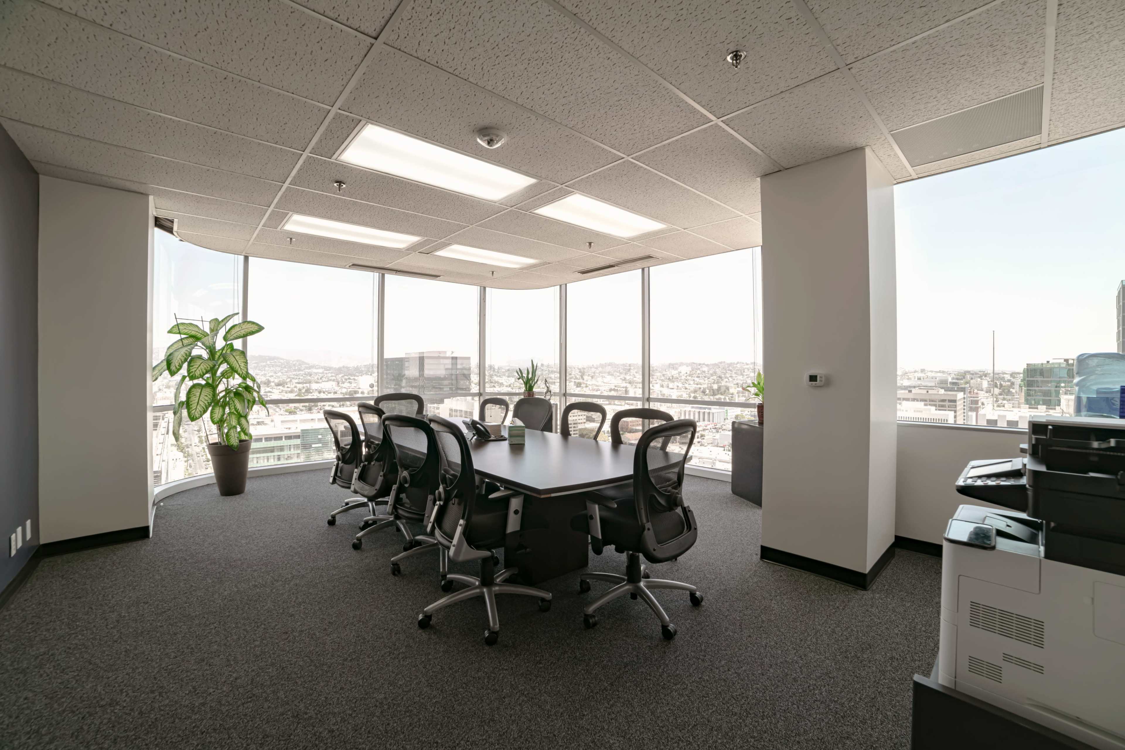 A modern conference room features a large table surrounded by ergonomic chairs, with floor-to-ceiling windows providing a view of the city skyline.