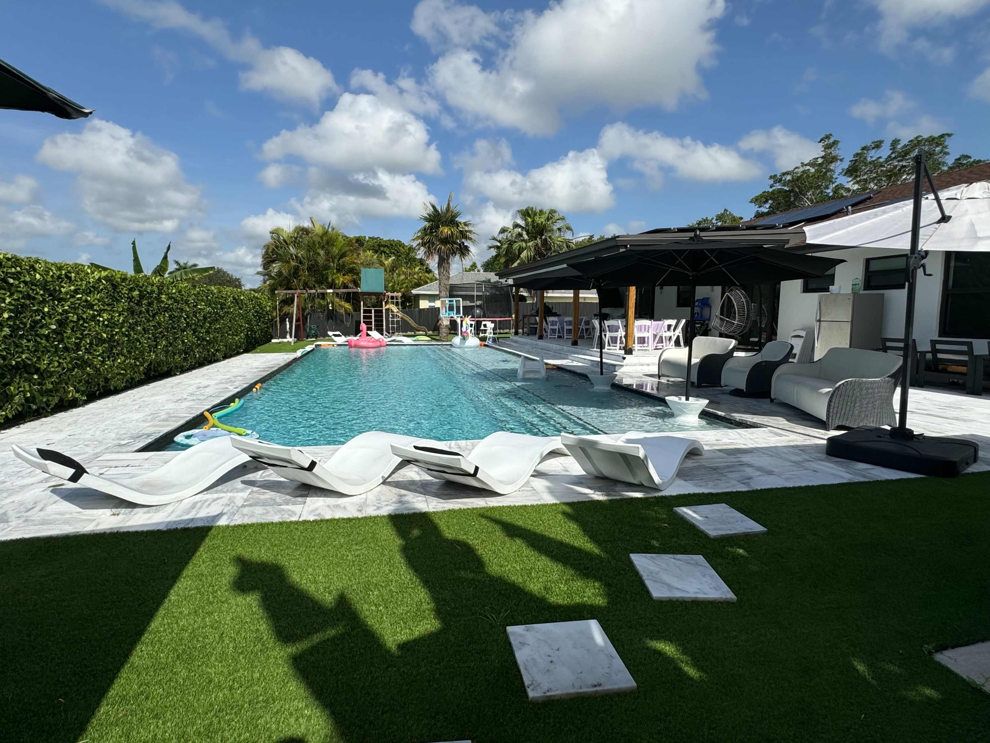 A swimming pool surrounded by lounging chairs, umbrellas, and landscaped greenery.
