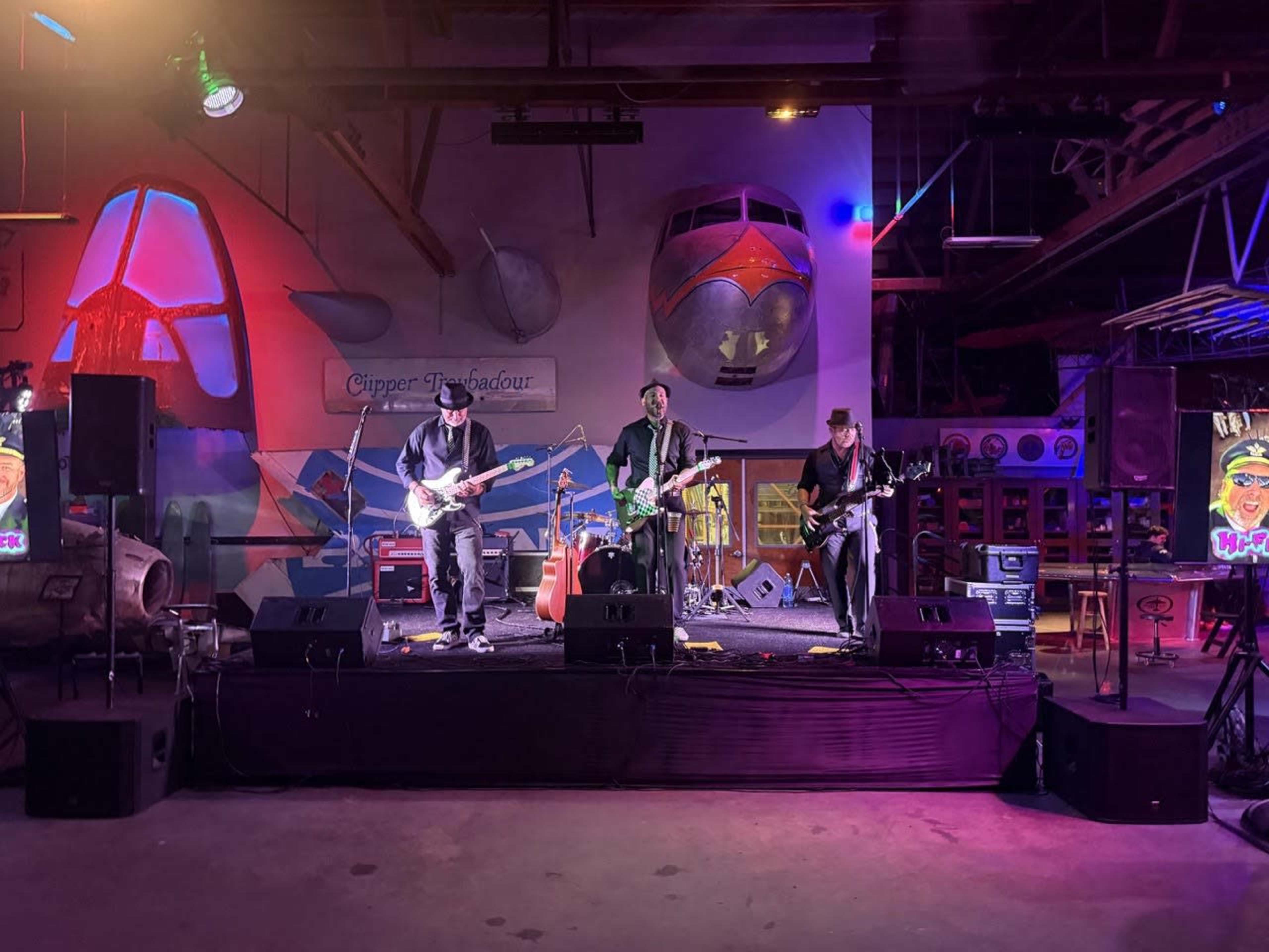 A band performs on stage in a venue adorned with colorful aircraft-themed decor.