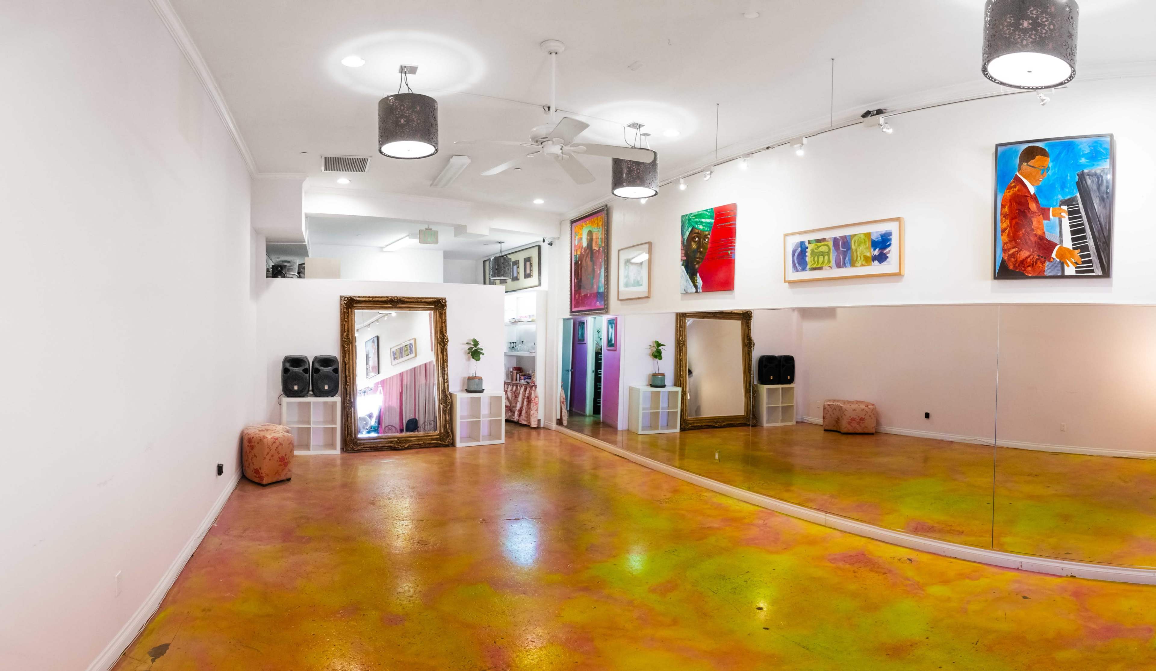 The image shows a brightly colored dance studio with a mirrored wall, vibrant floor, and several artworks displayed on the walls.