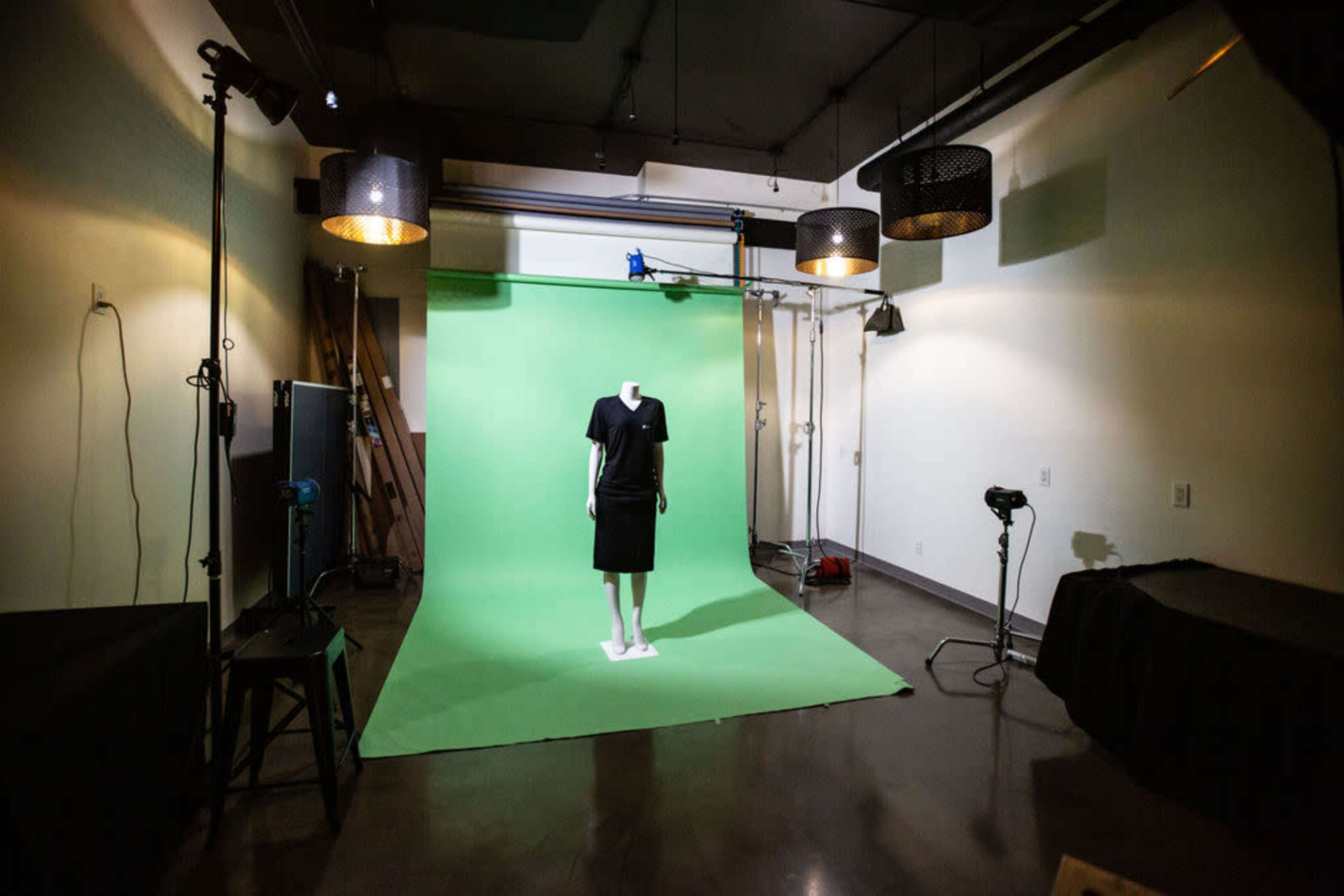 A mannequin dressed in a black outfit stands against a green backdrop in a well-lit studio space.