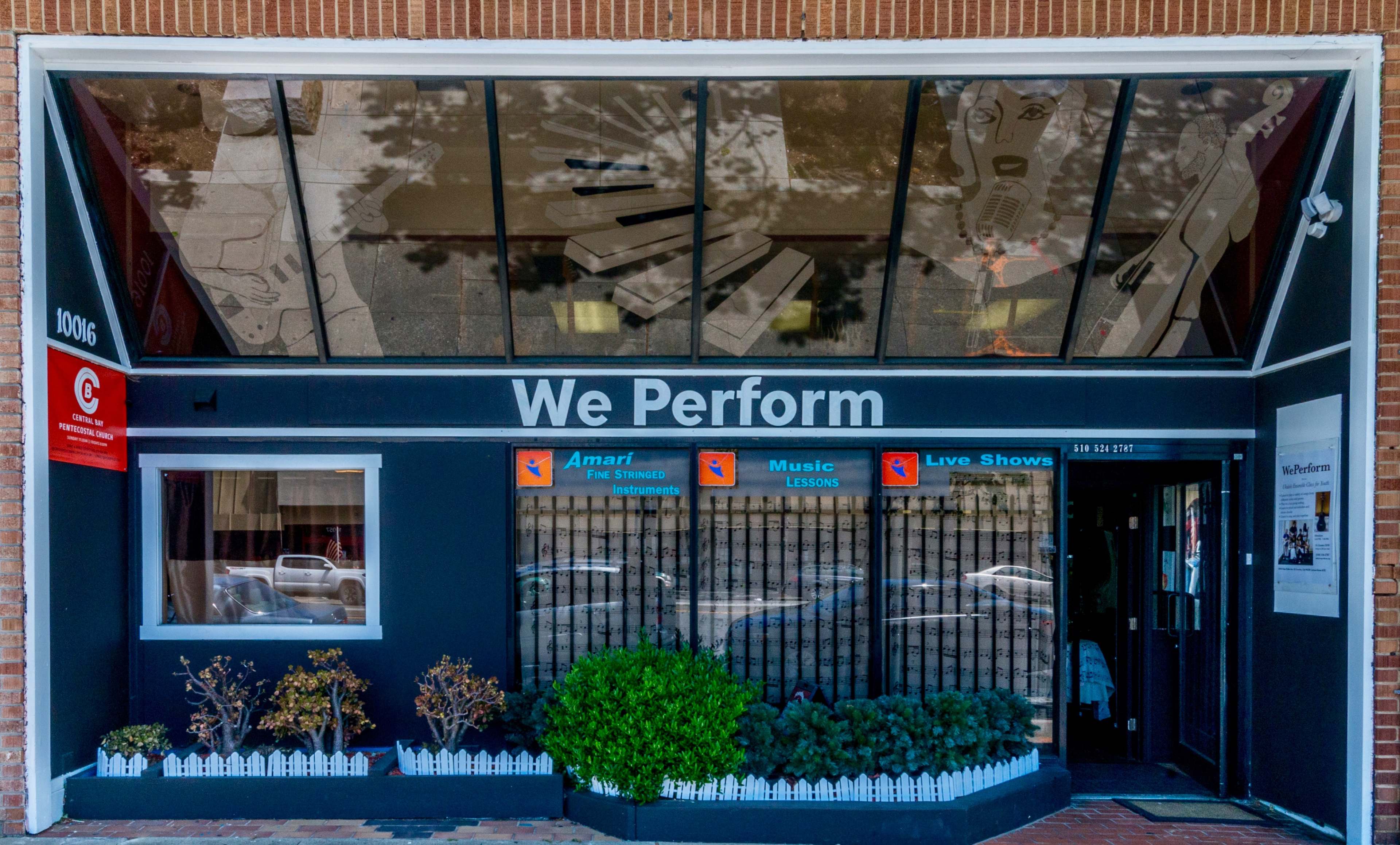 The image shows the entrance of a music and performance studio featuring a sign that reads "We Perform" and showcases a window display with artistic depictions of musical instruments and notes.