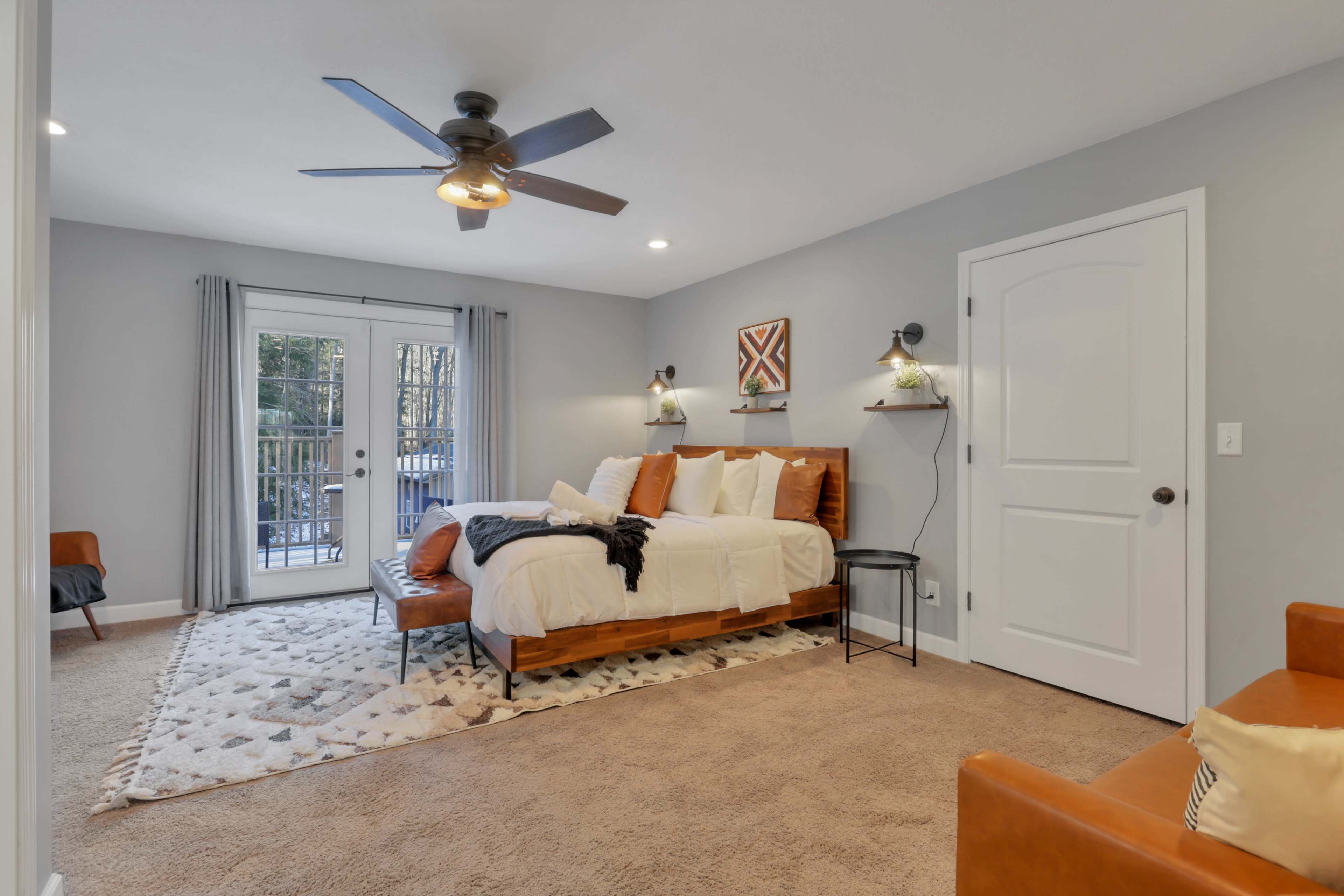 A spacious bedroom featuring a bed with white linens, a patterned area rug, and a set of sliding glass doors leading to a balcony.