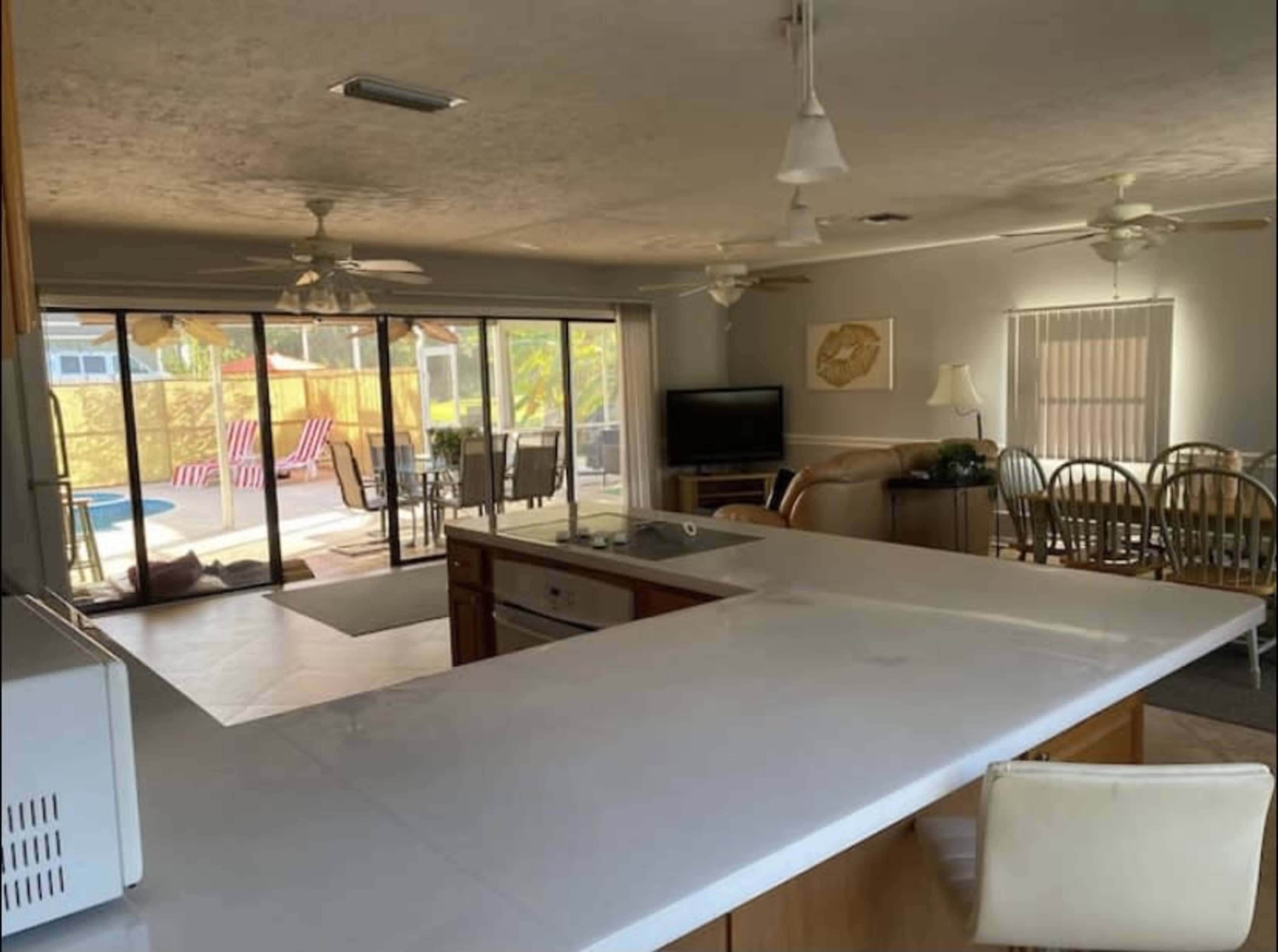 A spacious kitchen with a central island, open to a living area and a patio with outdoor furniture in the background.
