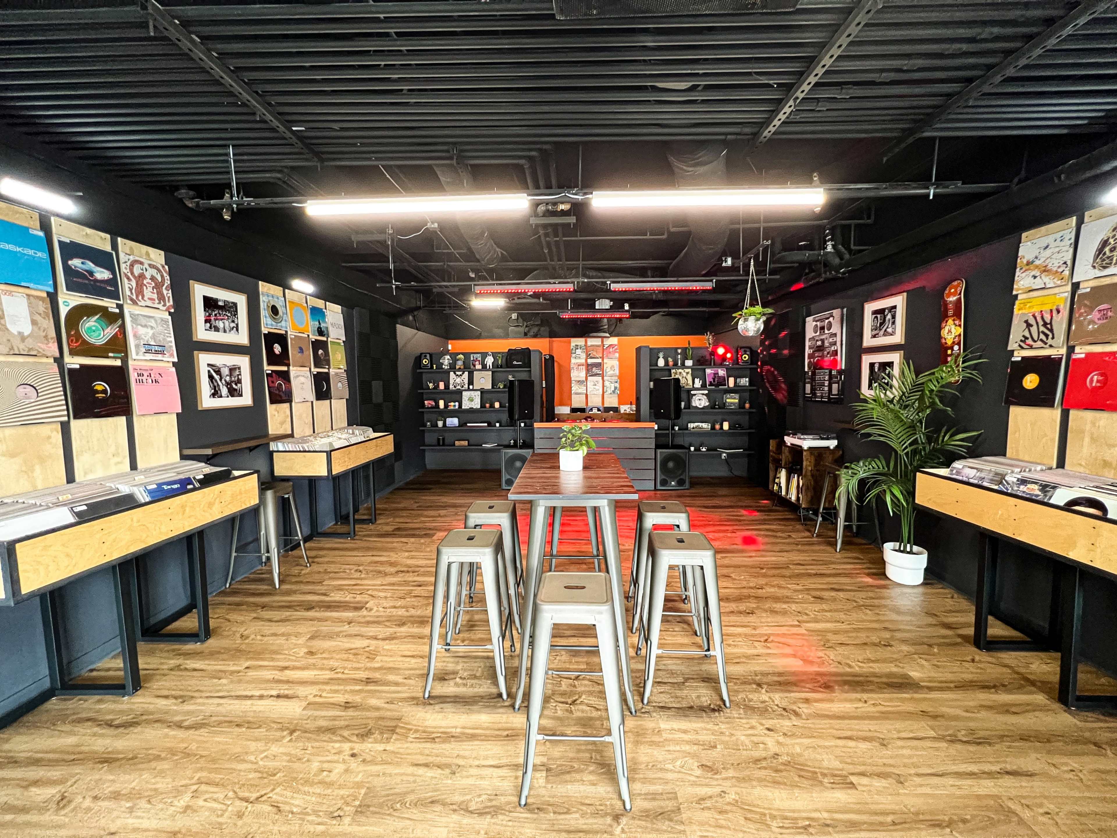 A modern shop featuring a display of vinyl records on the walls, a central table with metal stools, and a sleek, industrial interior design.
