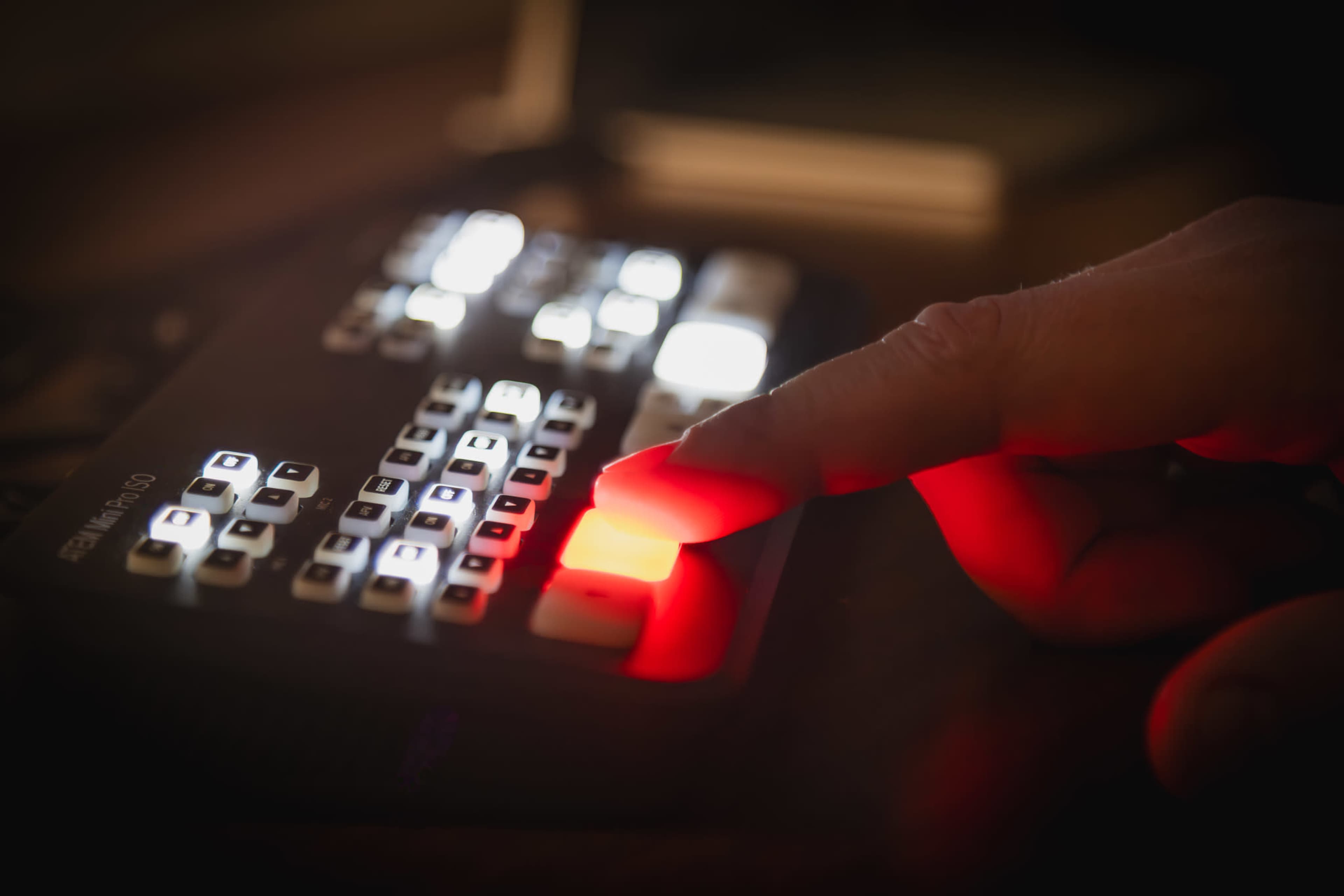 A hand presses a red button on a control panel filled with illuminated keys.