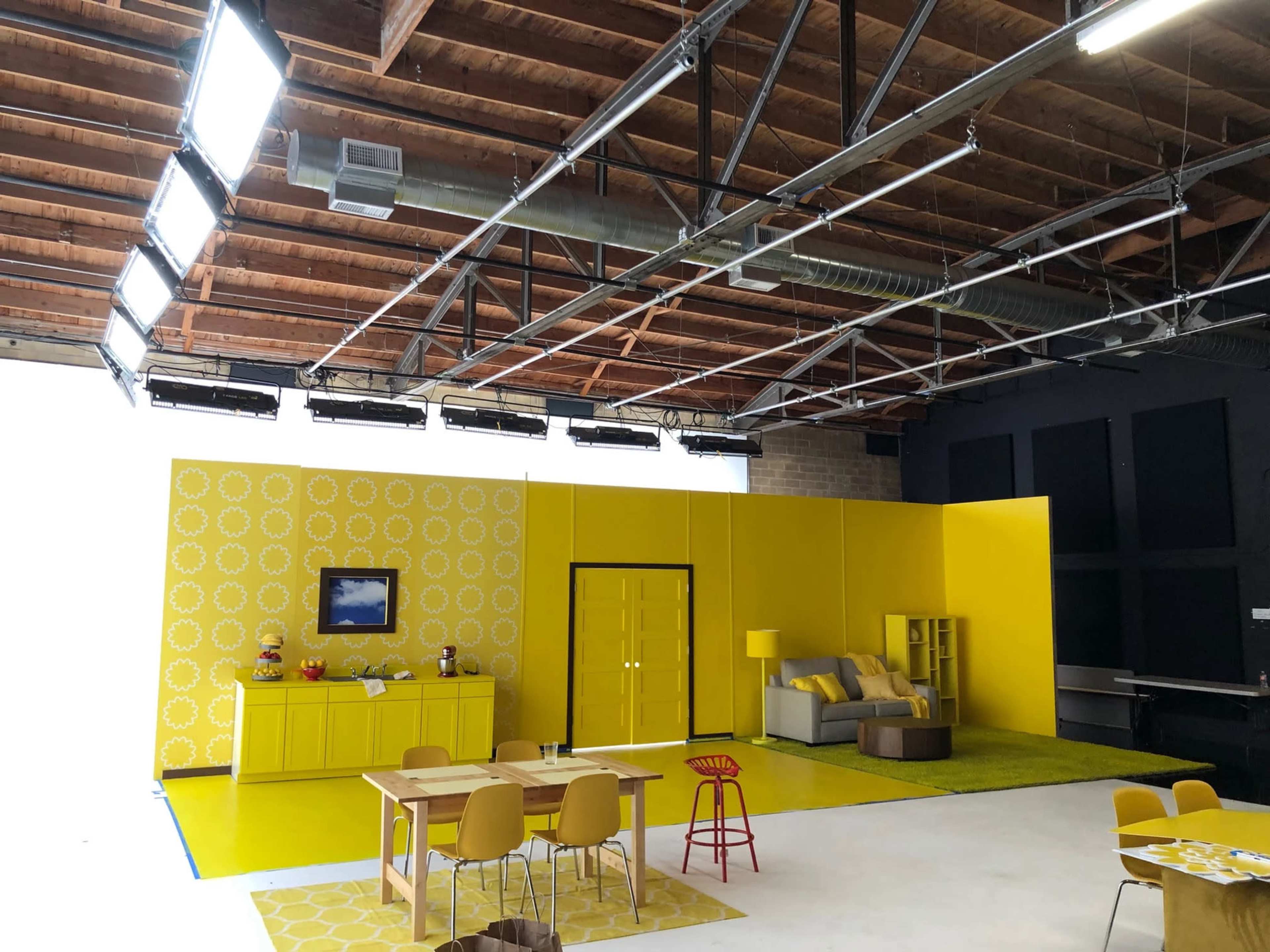 A brightly lit studio space featuring yellow walls, a couch, a table with chairs, and various decorative items.