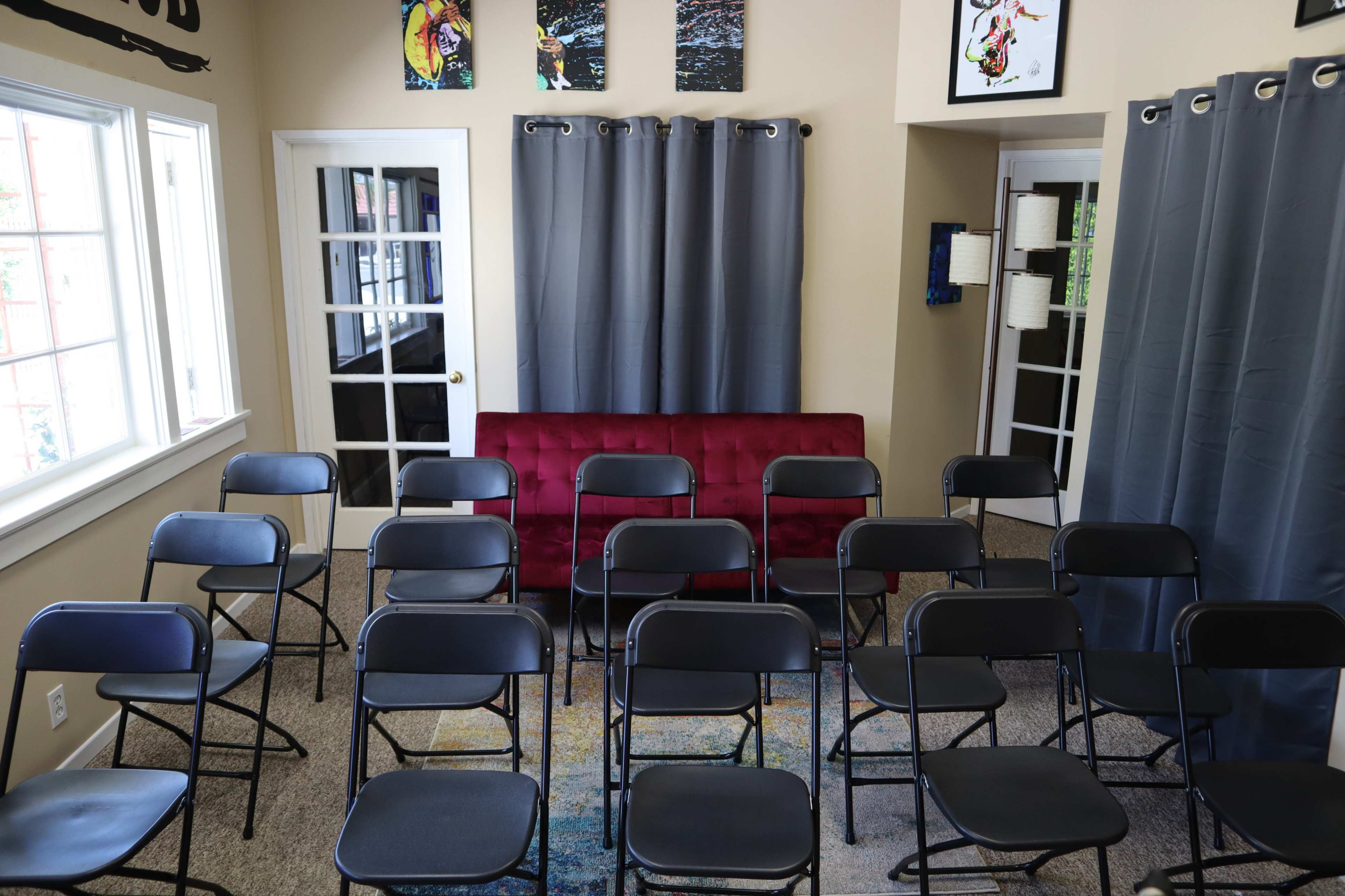 The room features a red couch against a wall with gray curtains, surrounded by a set of black folding chairs arranged in rows on a carpeted floor.