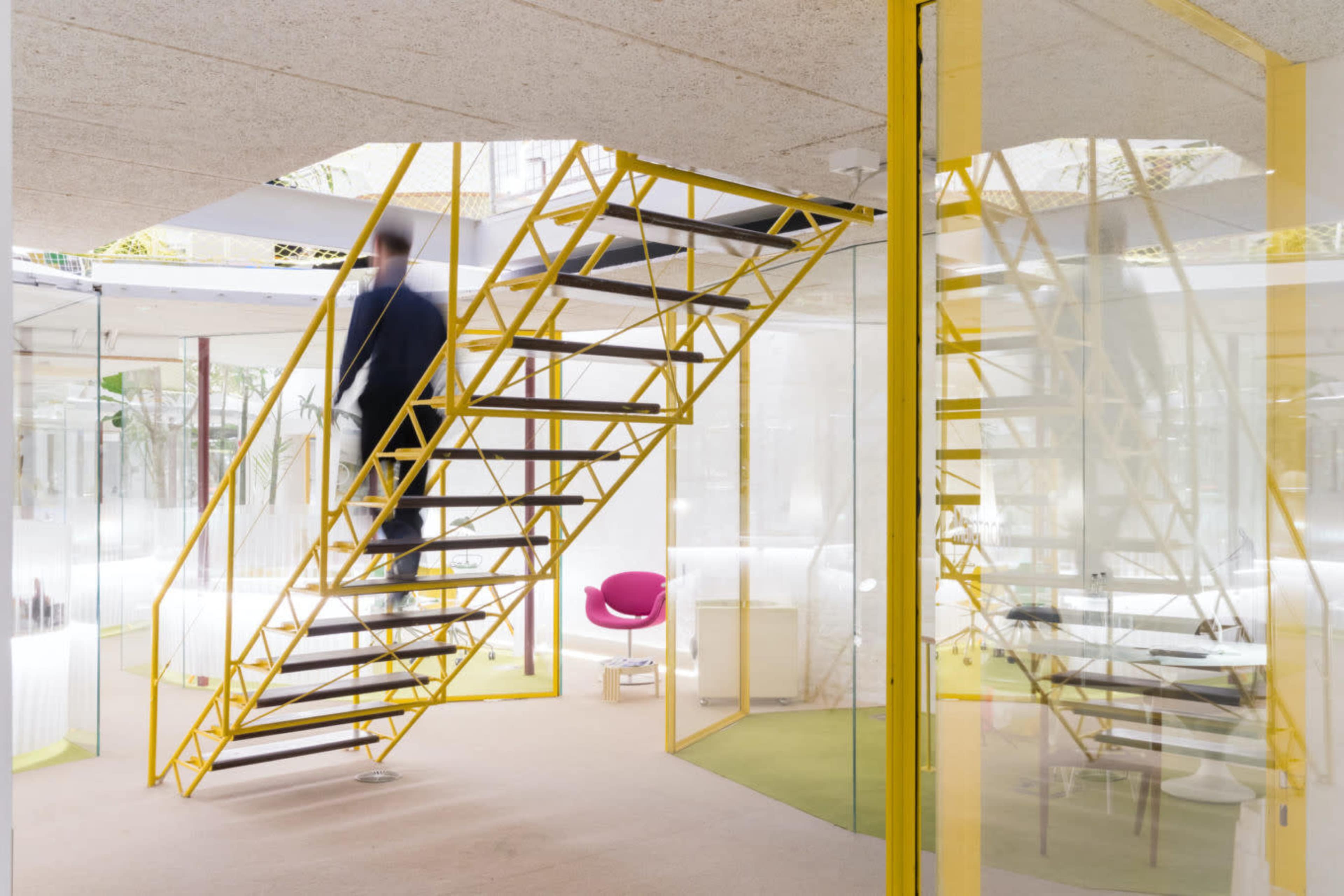 A person walks up a yellow staircase in a modern, glass-enclosed space.