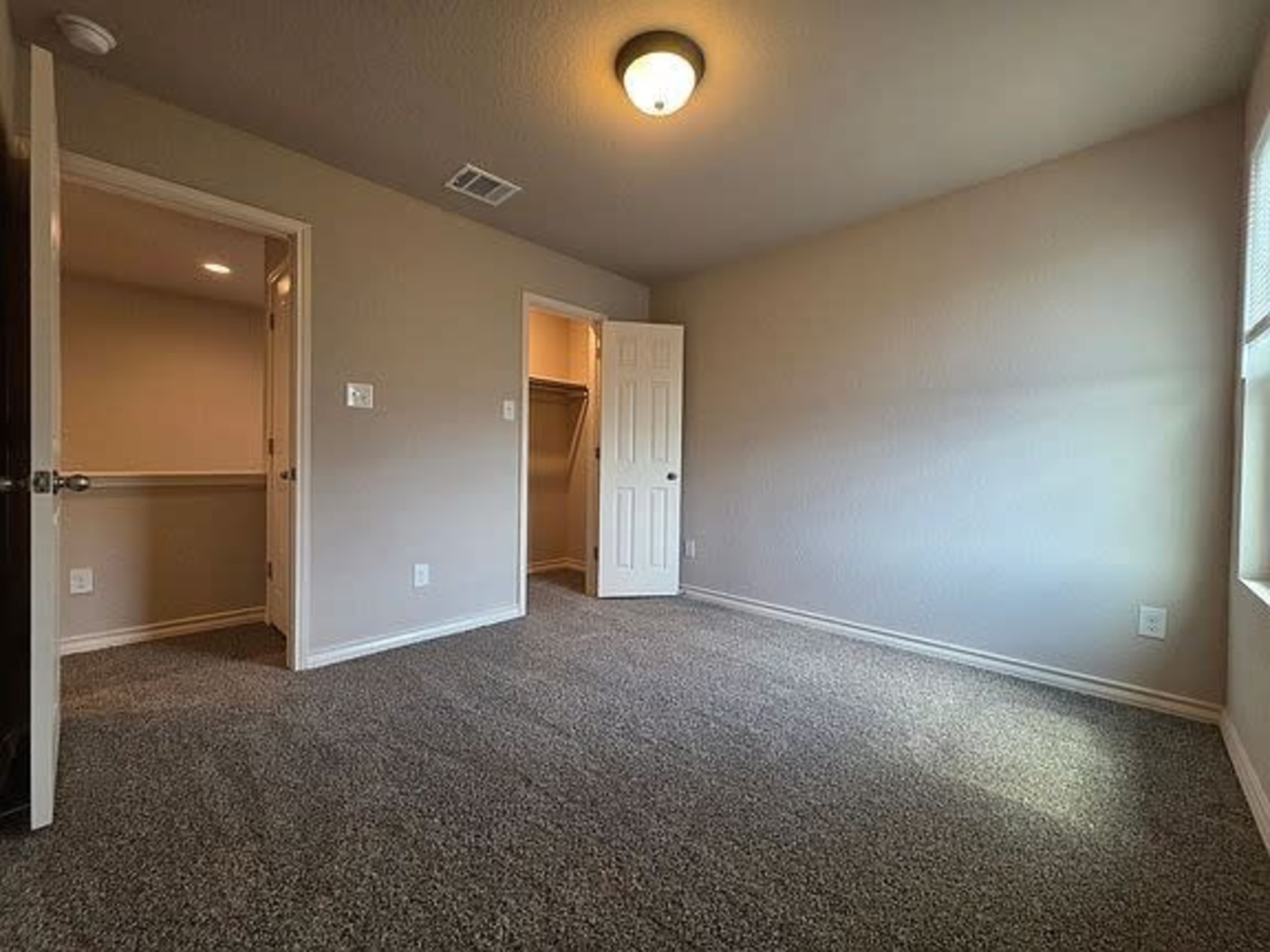 The image shows a sparsely furnished room with beige walls, a light fixture, and a doorway leading to a closet.
