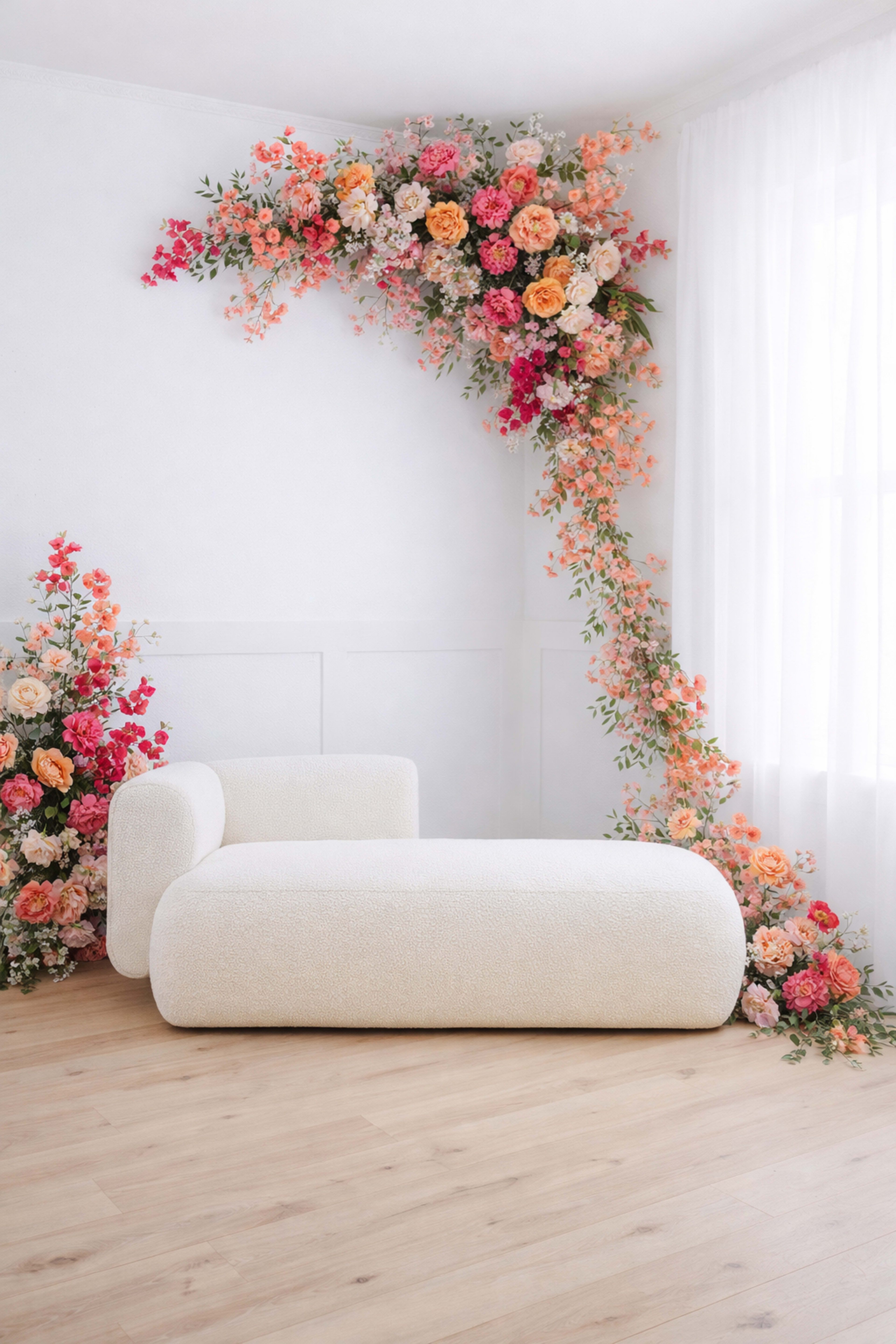 A minimalist room features a white sculptural sofa adjacent to a floral arrangement arching from the wall.