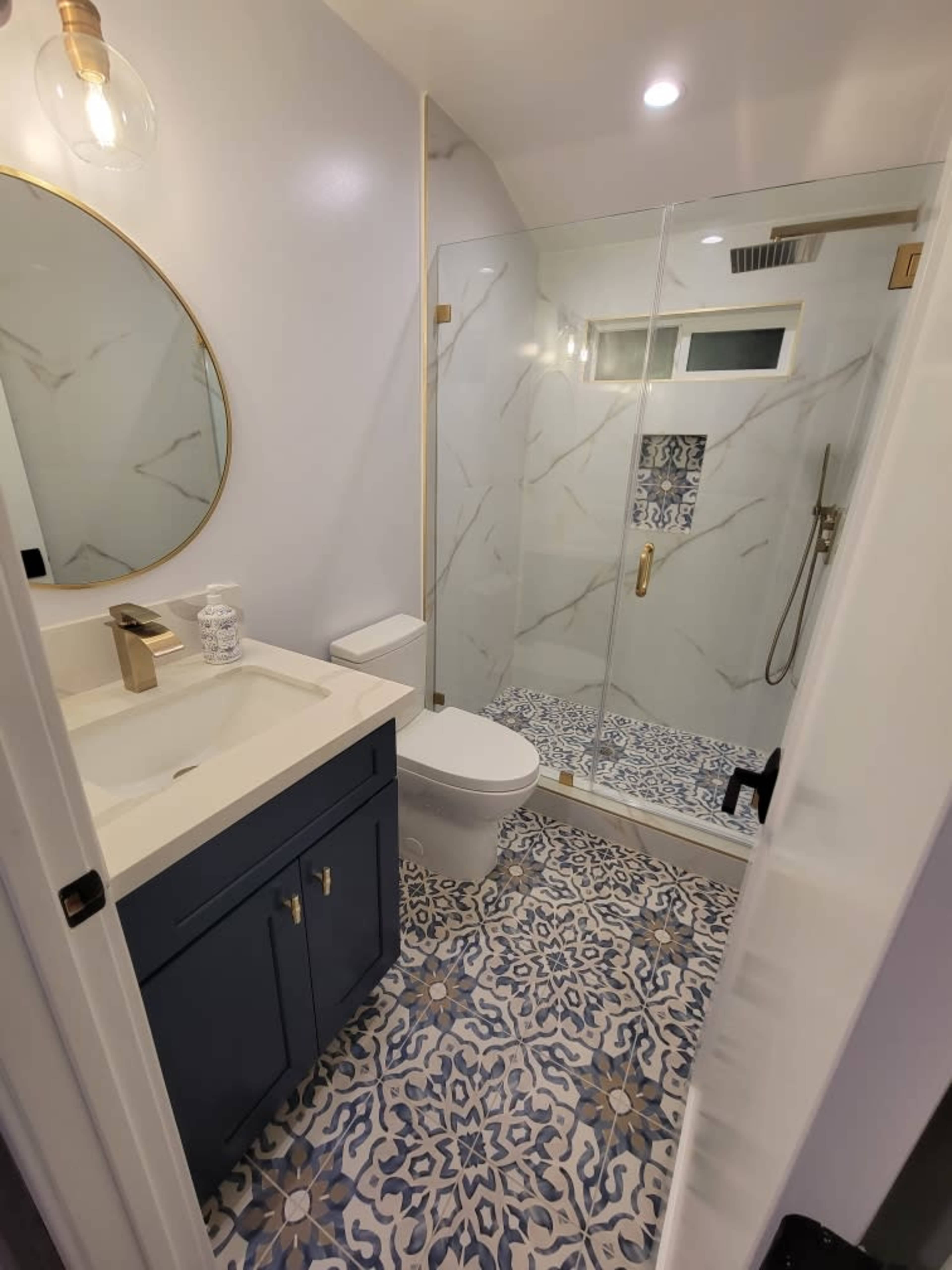 A modern bathroom featuring a glass shower, a white toilet, a stylish sink with a dark blue vanity, and patterned tile flooring.